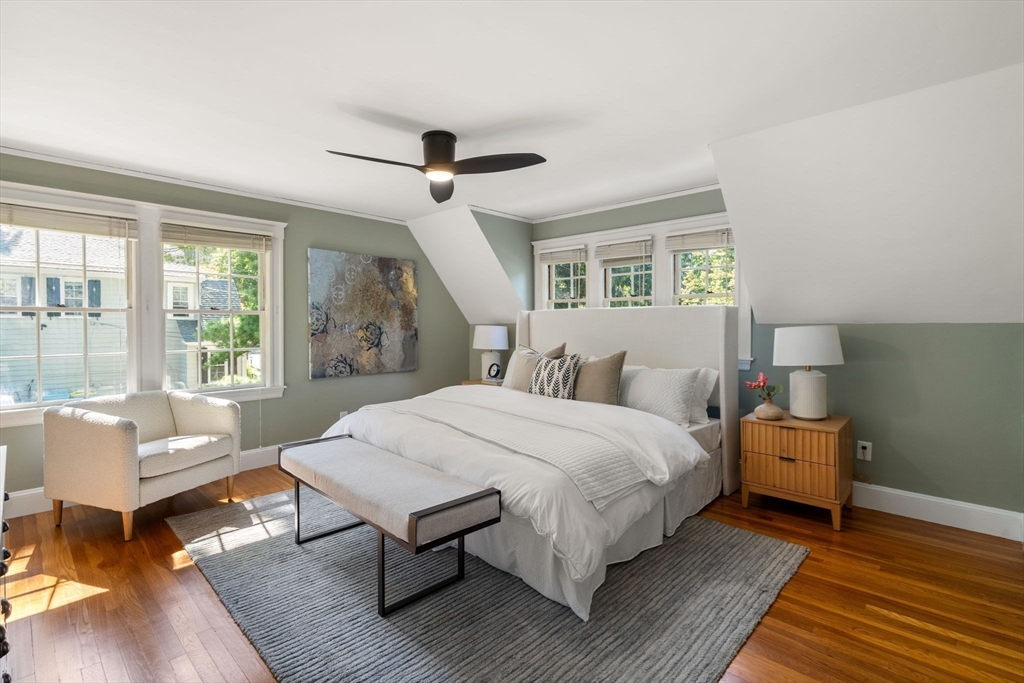 Bedroom with a large white bed, sage-green walls, sloped ceiling, and hardwood floors.