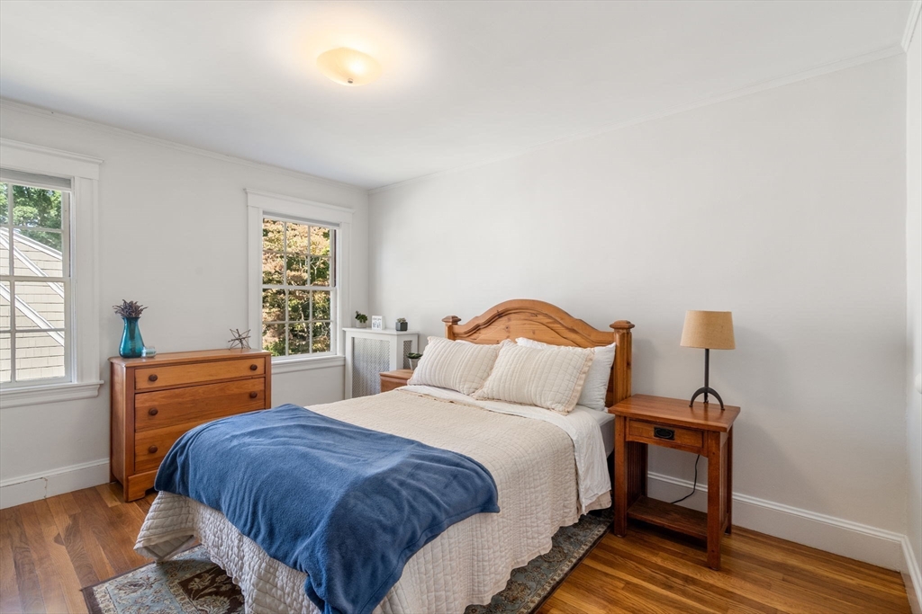 Bedroom with a wooden bed, white bedding, blue throw, and hardwood floors.