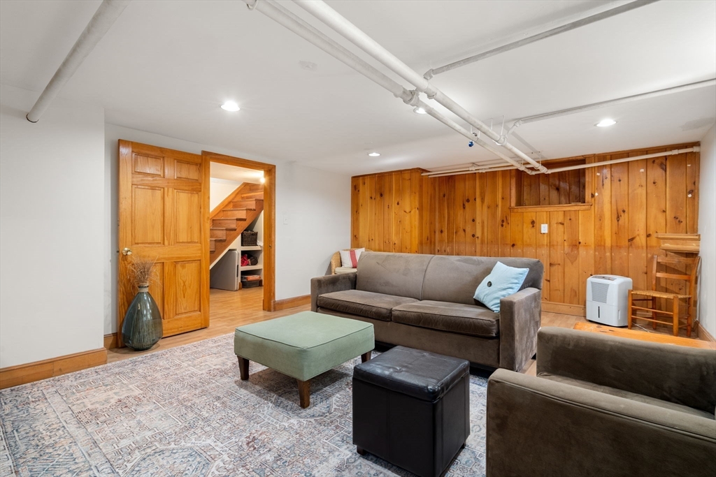 Furnished basement family room with wood-paneled walls, a seating area, and exposed ceiling pipes.