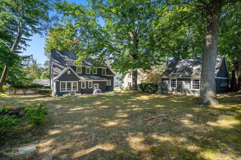 Dark gray house and detached garage behind a grassy yard shaded by mature trees.