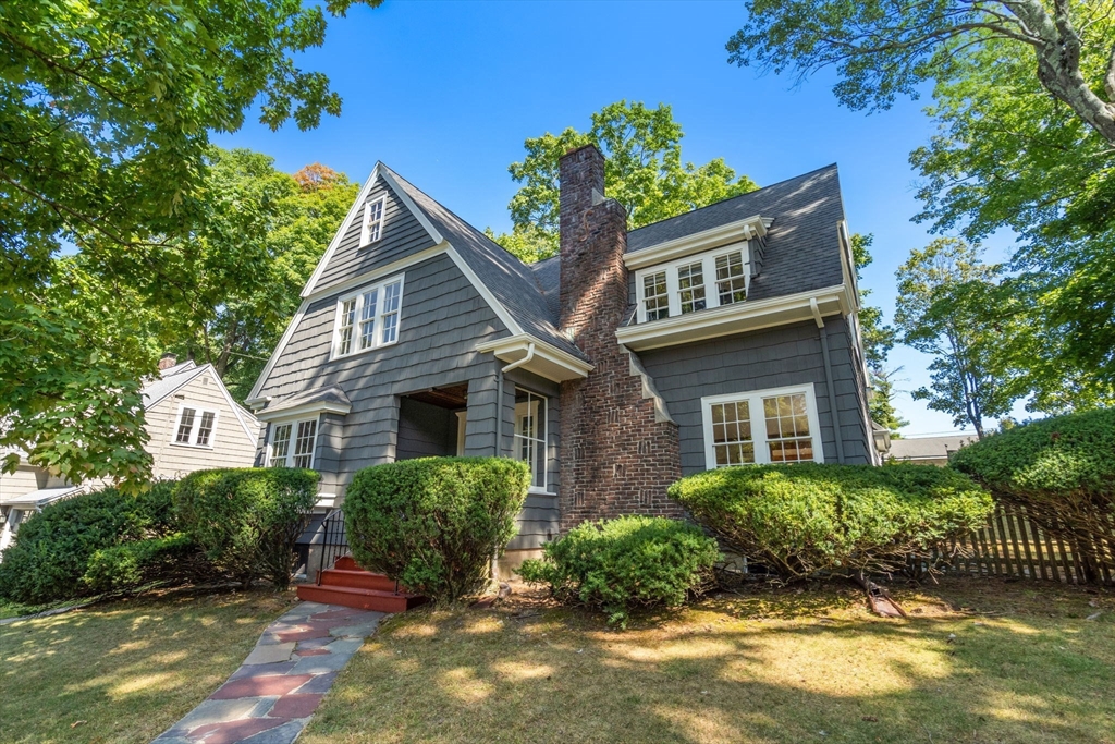 Dark gray shingle-sided house with steep gables, a tall brick chimney, and landscaped front entry.