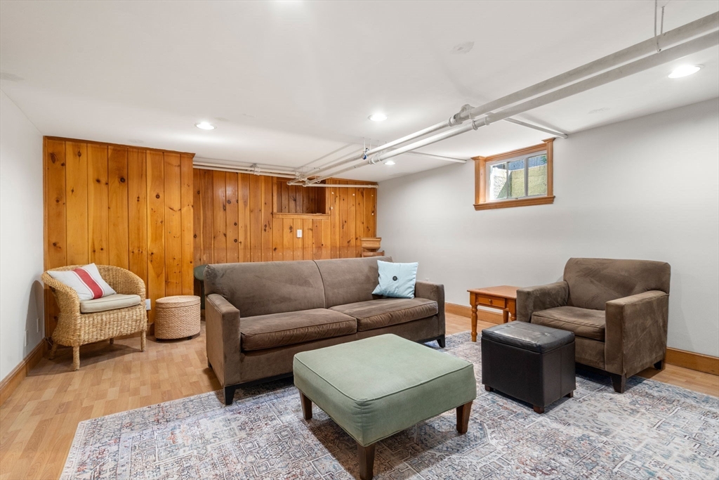 Basement family room with brown seating, a patterned rug, and a honey-colored wood-paneled wall.