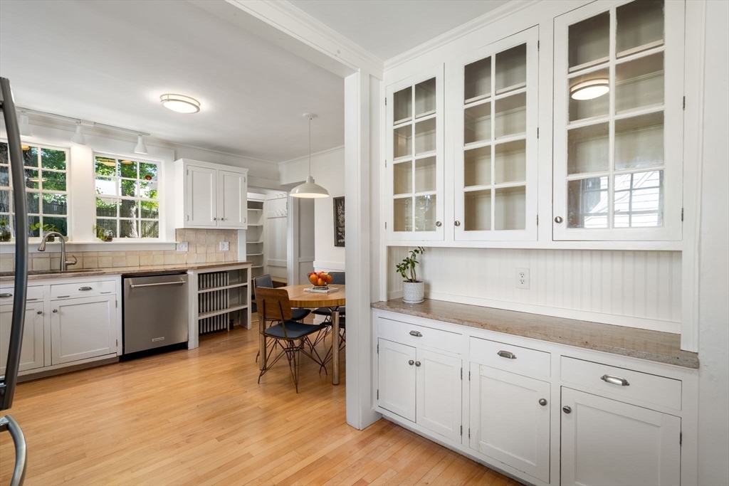 Bright white kitchen with glass-front cabinets, hardwood floors, and a small dining area.