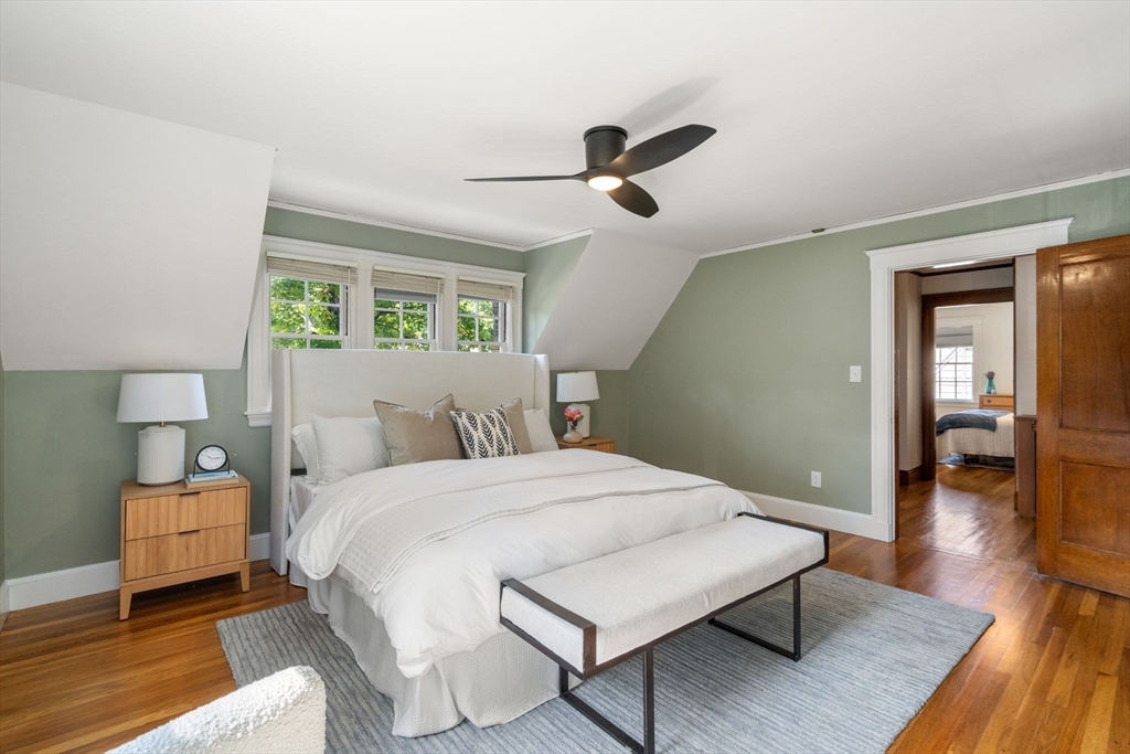 Bedroom with a white bed, upholstered bench, sage-green walls, and hardwood floors.