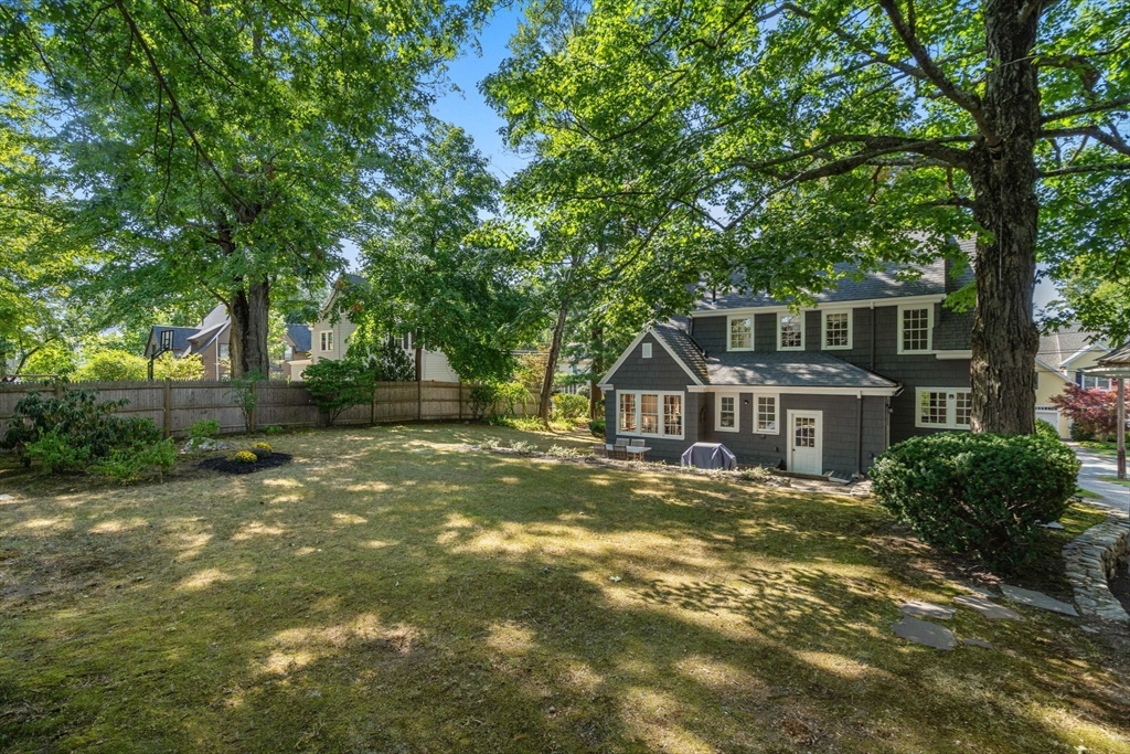 Rear of a gray two-story house beyond a broad lawn shaded by mature trees.