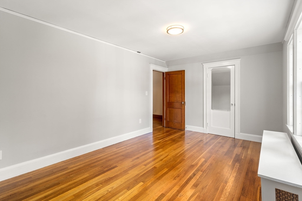 Empty room with polished hardwood floors, a large window, and a white closet door.