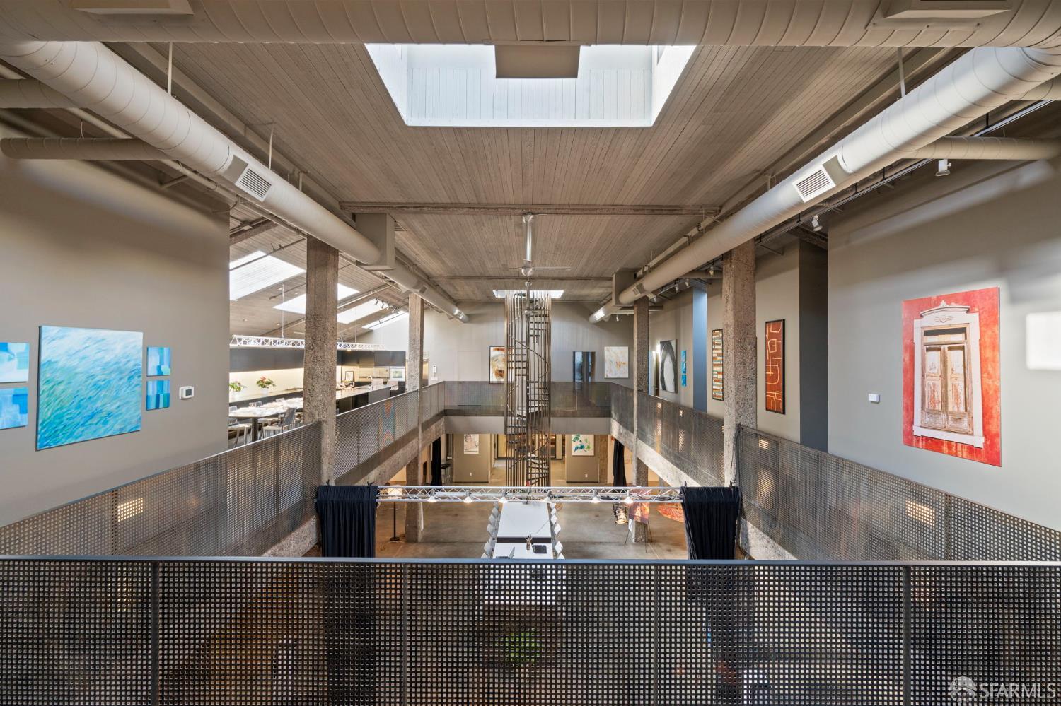 Multi-level industrial interior with a central atrium, metal mezzanine railings, exposed ducts, and wall art.