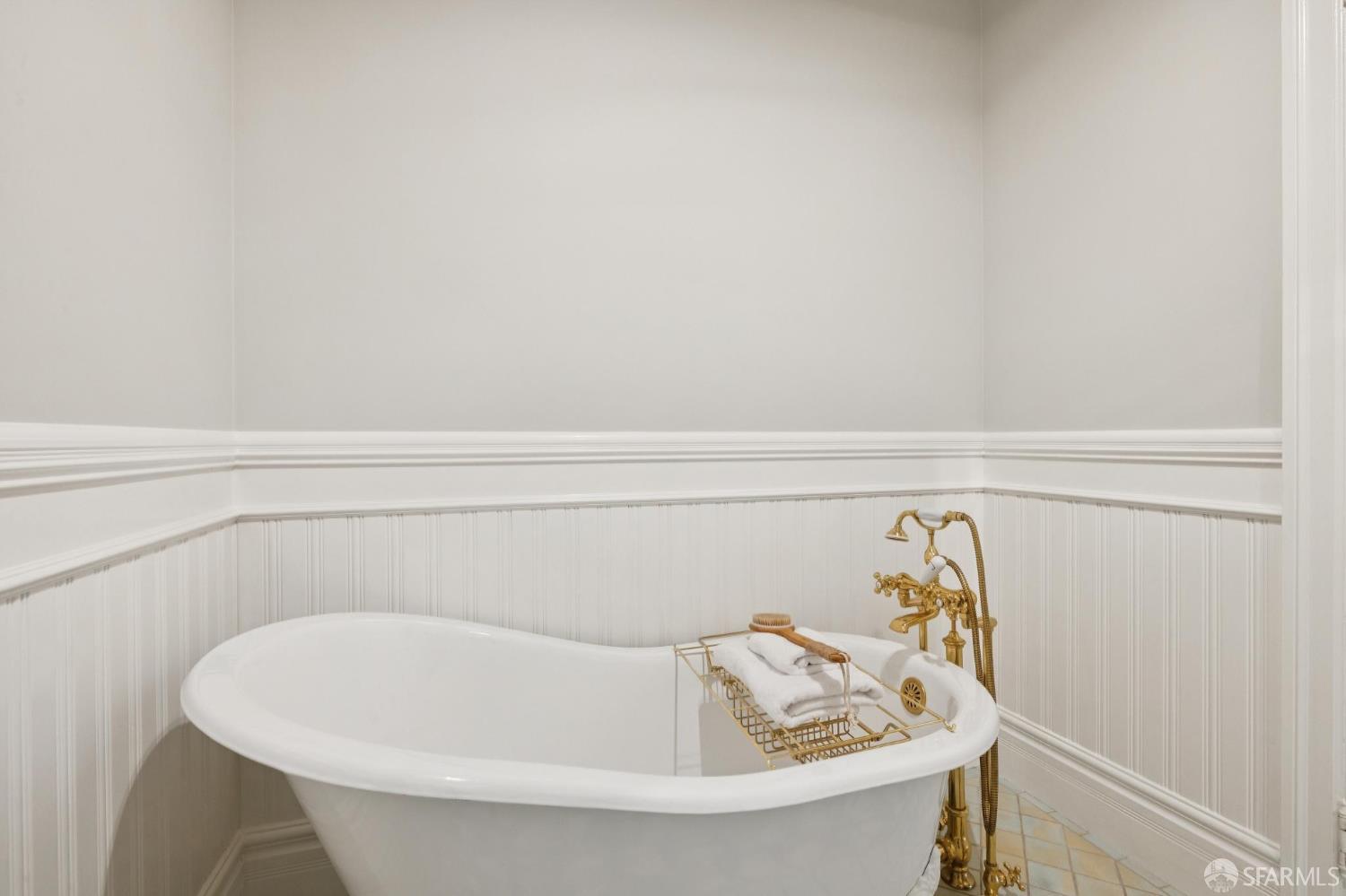 Freestanding bathtub with ornate gold fixtures and folded towels on a brass rack.