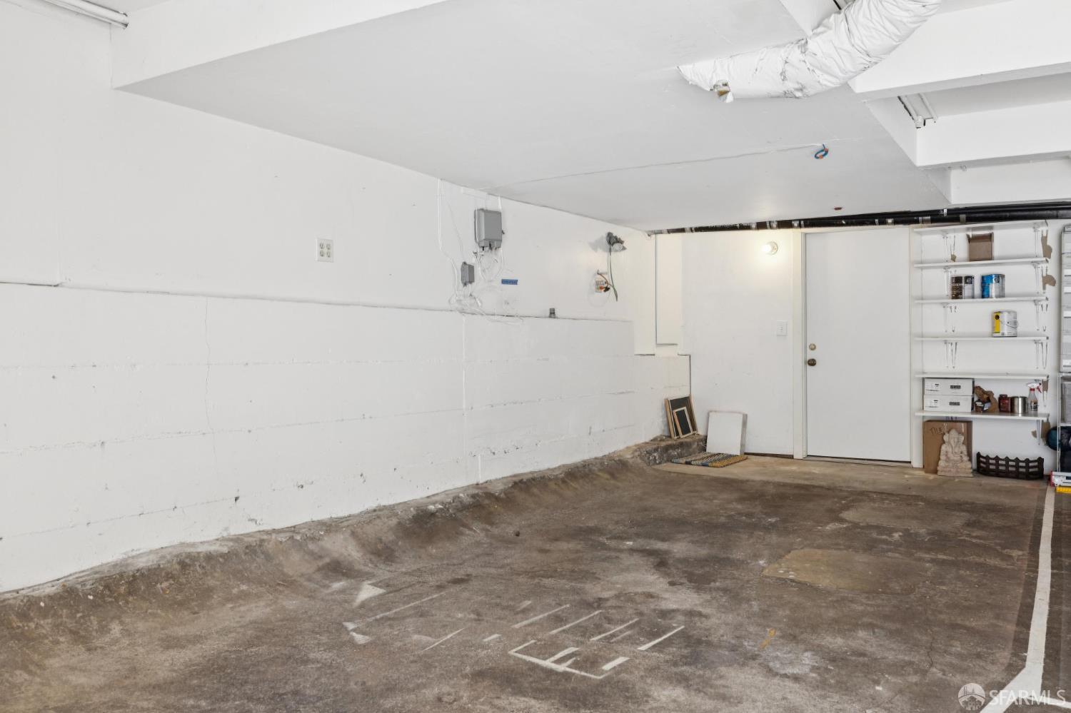 Garage parking space with a worn concrete floor and storage shelves along one wall.