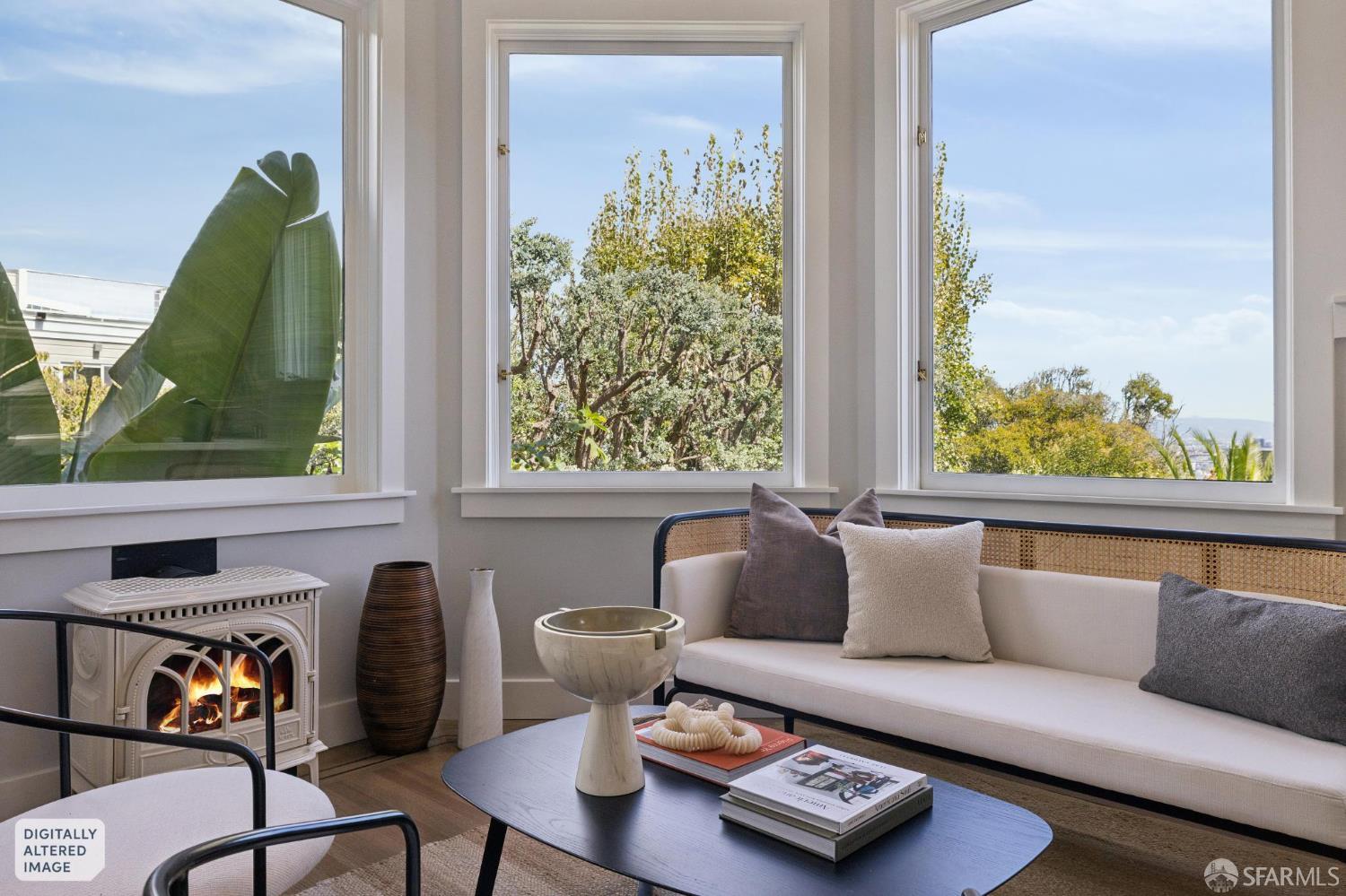 Living room with a decorative fireplace, white sofa, and large windows overlooking trees.