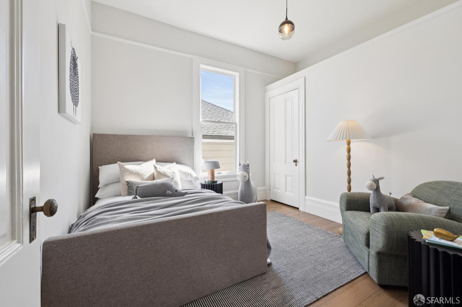 Bright bedroom with a gray upholstered bed, striped rug, and green armchair beside a narrow window.