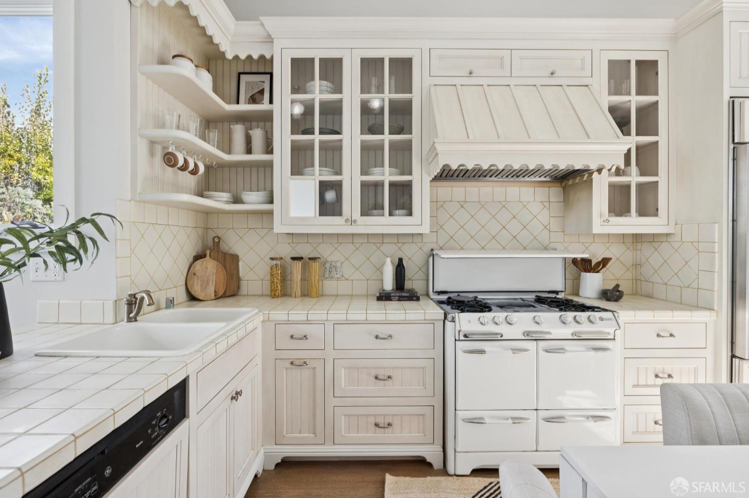 Bright white kitchen with a farmhouse range, paneled hood, and cream tile counters.