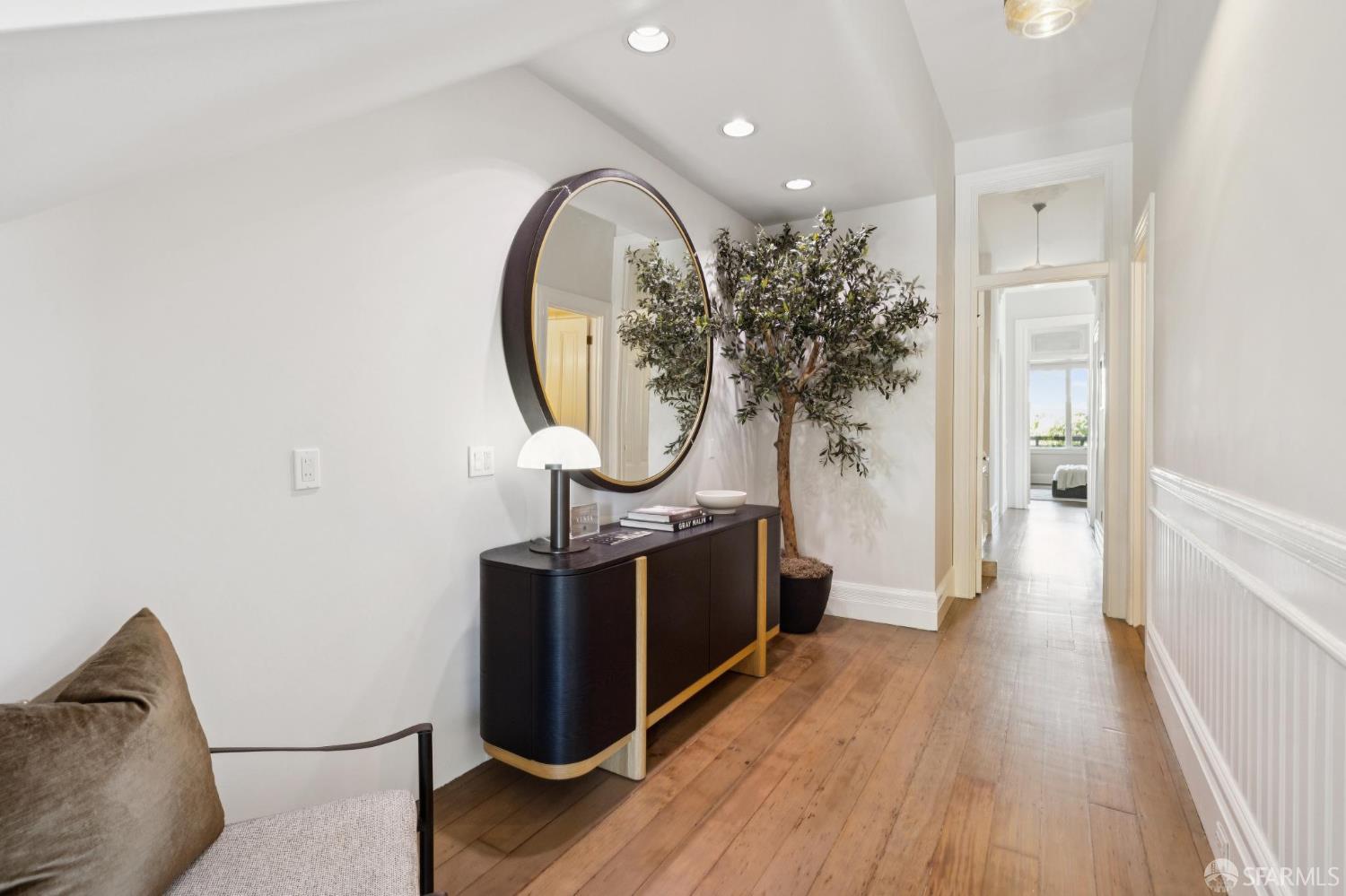Furnished entry hallway with wood floors, a round mirror, and a dark console beside a potted tree.