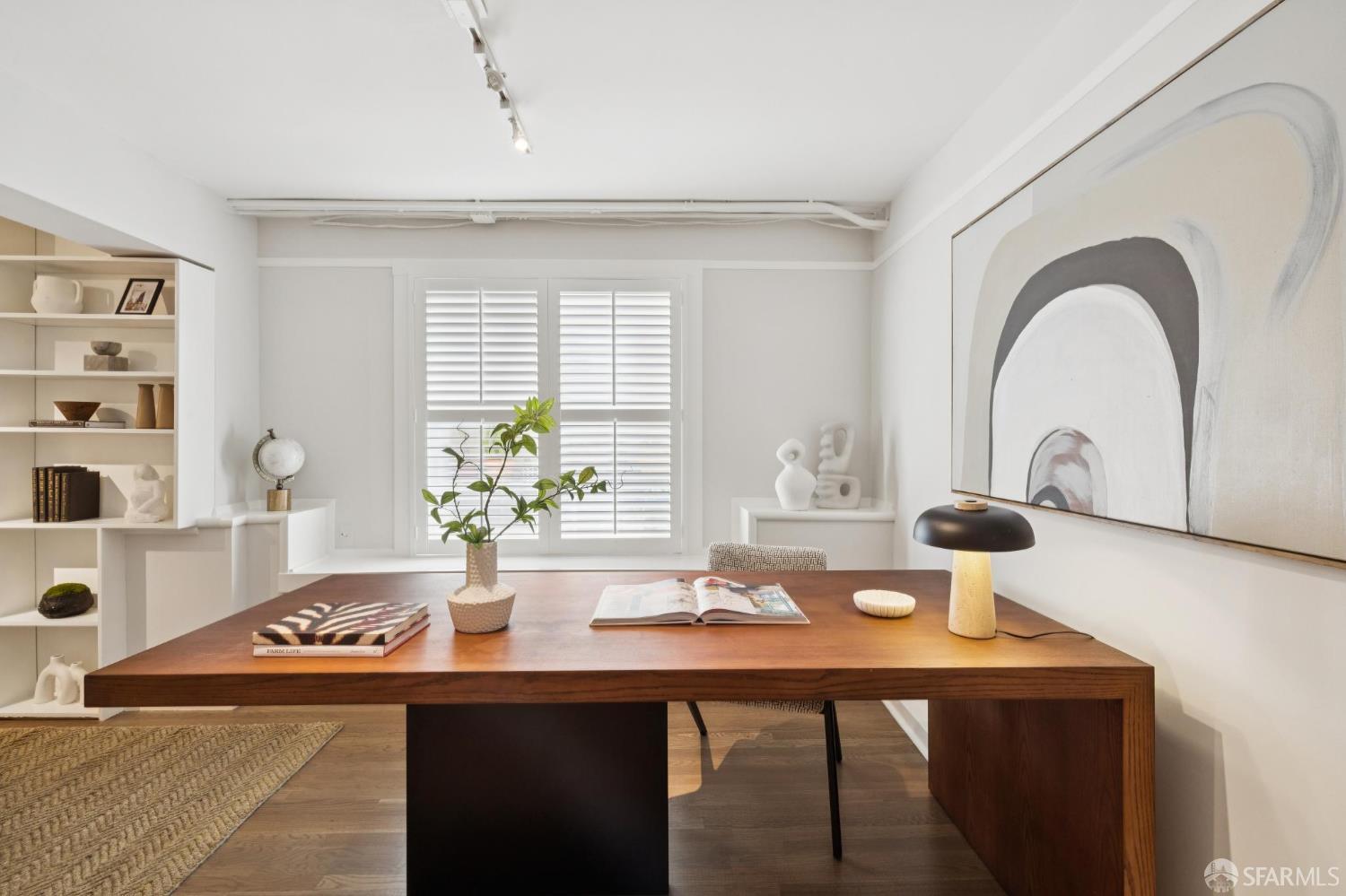 Home office with a large wooden desk, shuttered window, built-in shelves, and oversized abstract artwork.