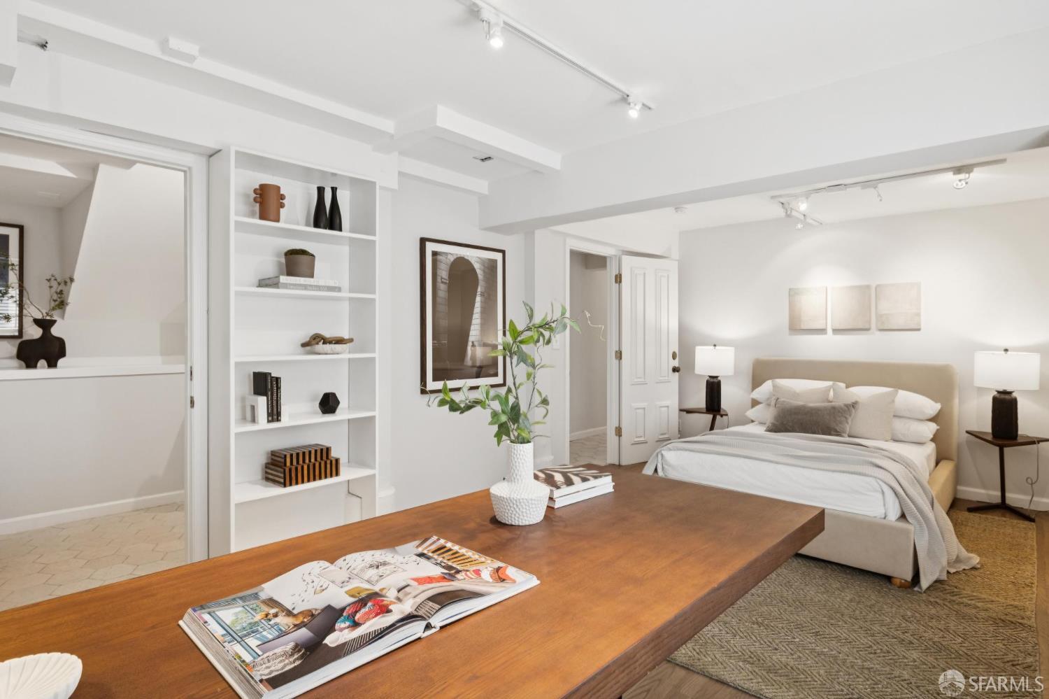 Staged bedroom with a beige bed, built-in shelves, and a long wooden table.