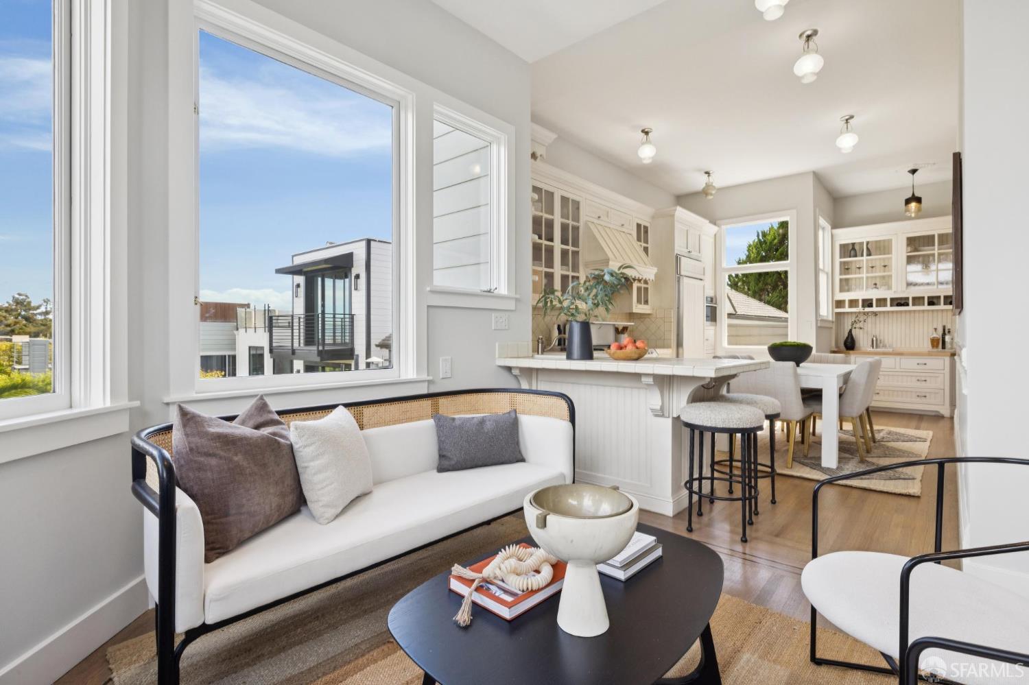 Living room with a white sofa beside an open kitchen and dining area, framed by large windows.