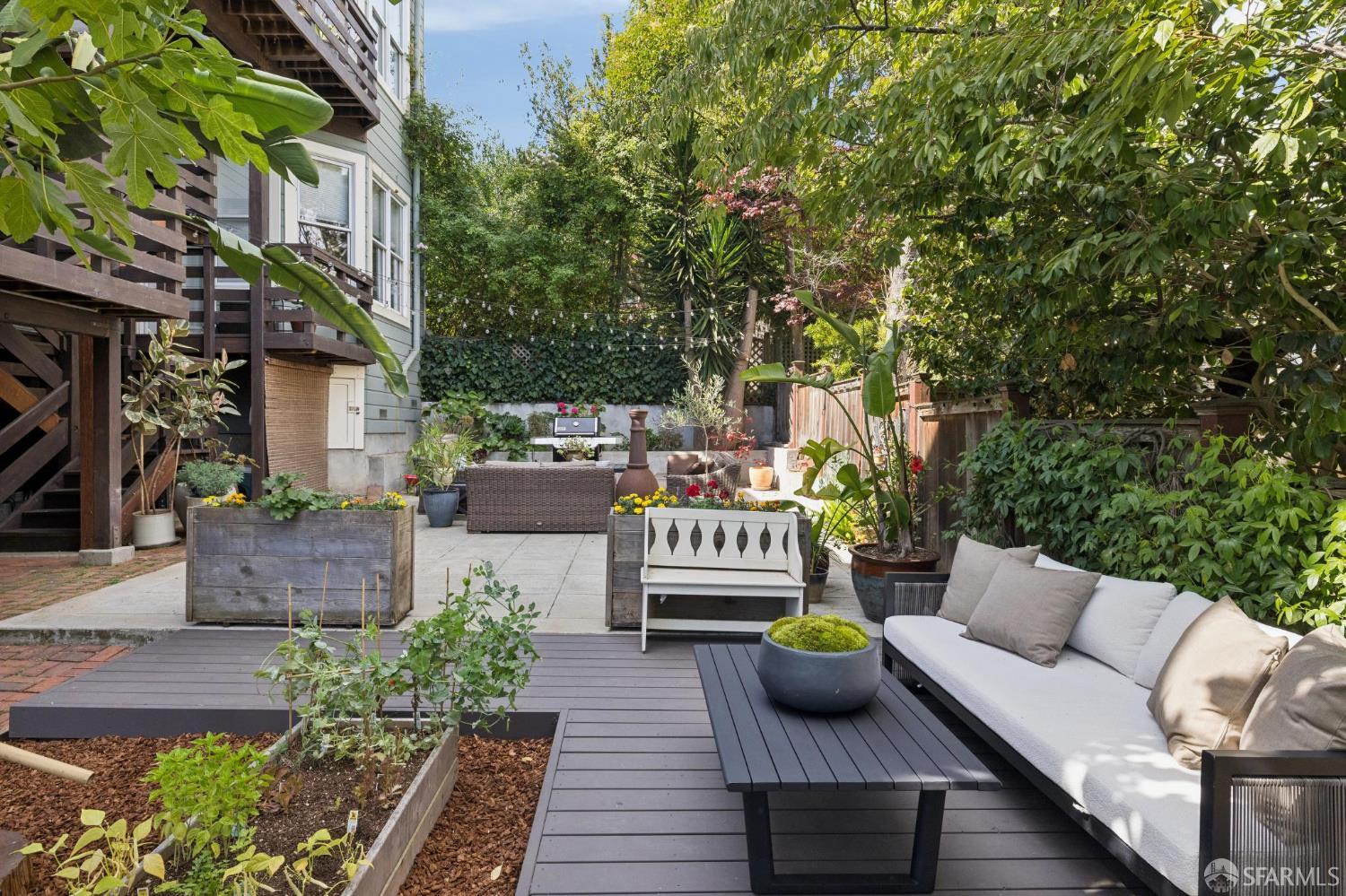 Landscaped backyard patio with a gray deck, raised planters, and outdoor seating.