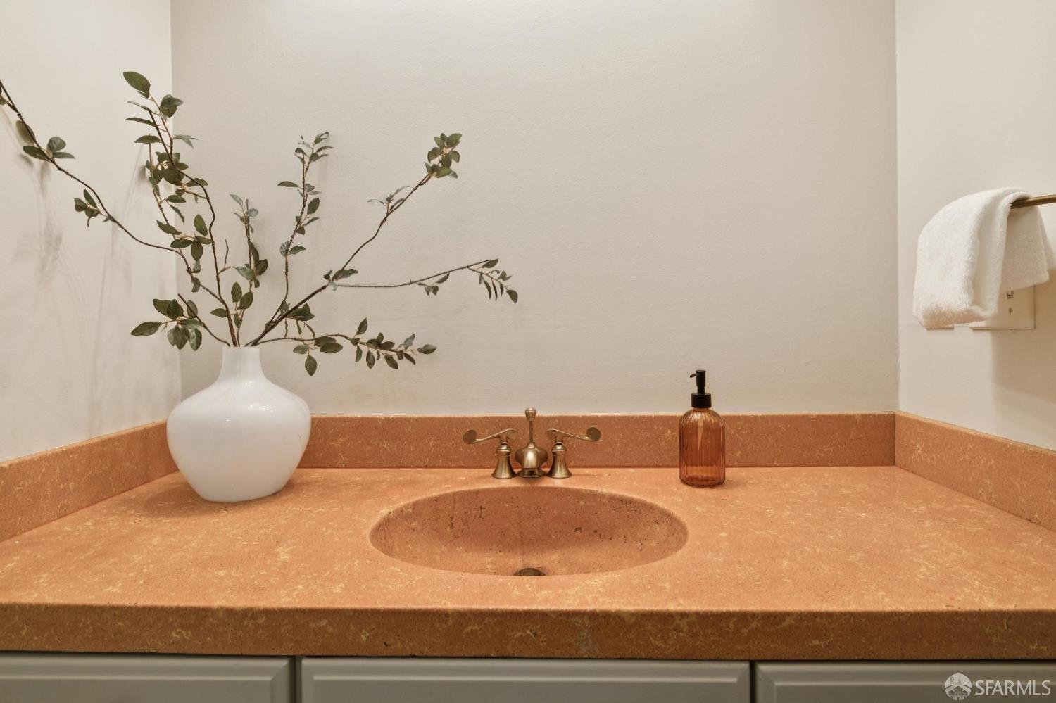 Bathroom vanity with a salmon-colored stone counter, integrated sink, brass faucet, and leafy branches in a vase.