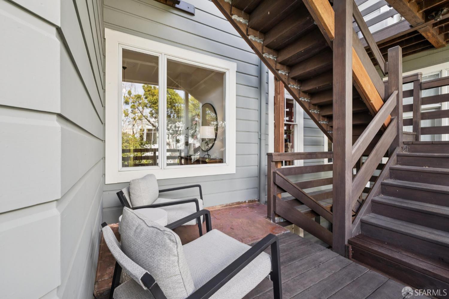 Outdoor deck with cushioned chairs beside dark wood stairs and gray siding.