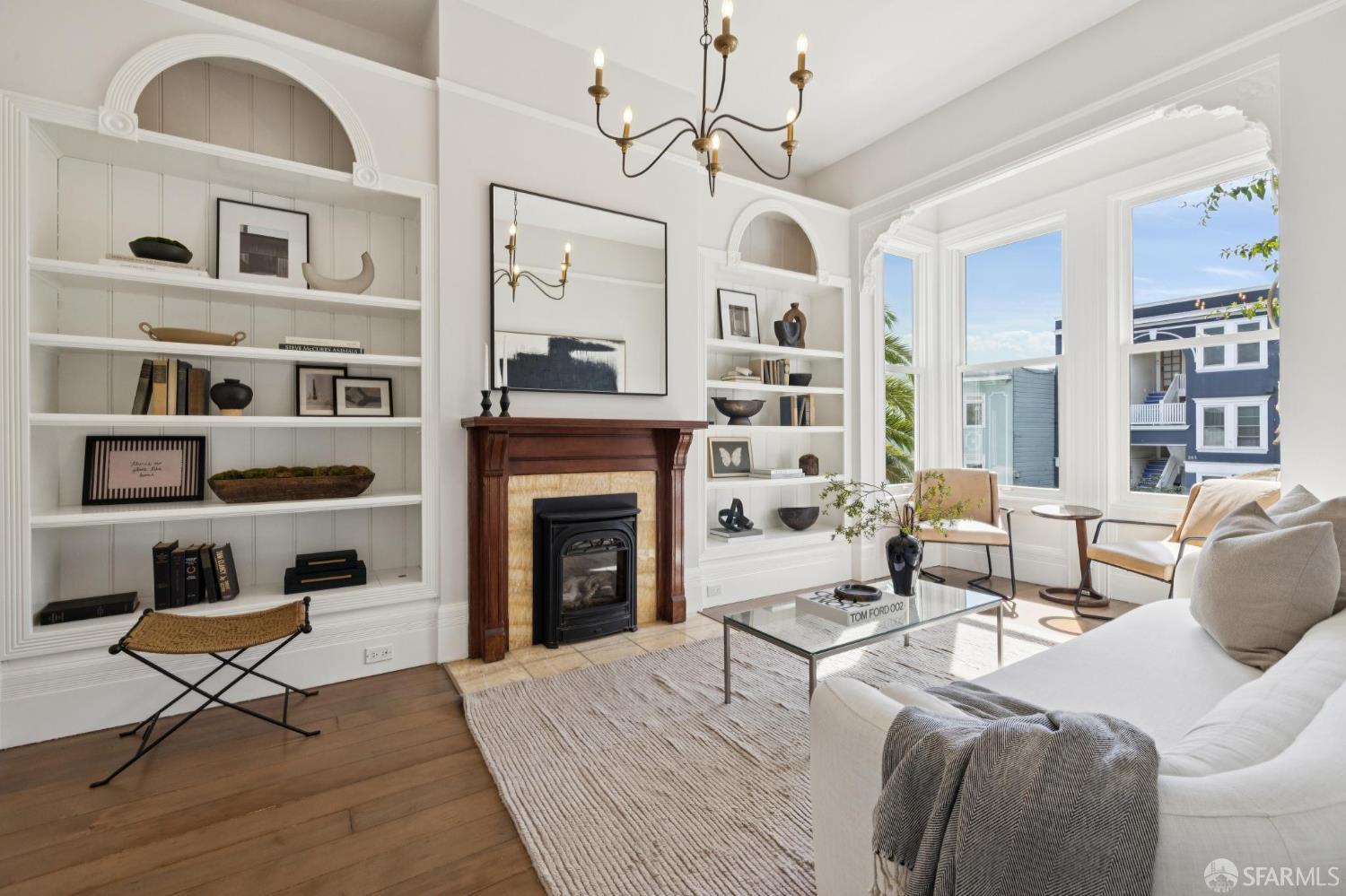 Living room with built-in bookshelves, a wood-trimmed fireplace, and large sunny windows.