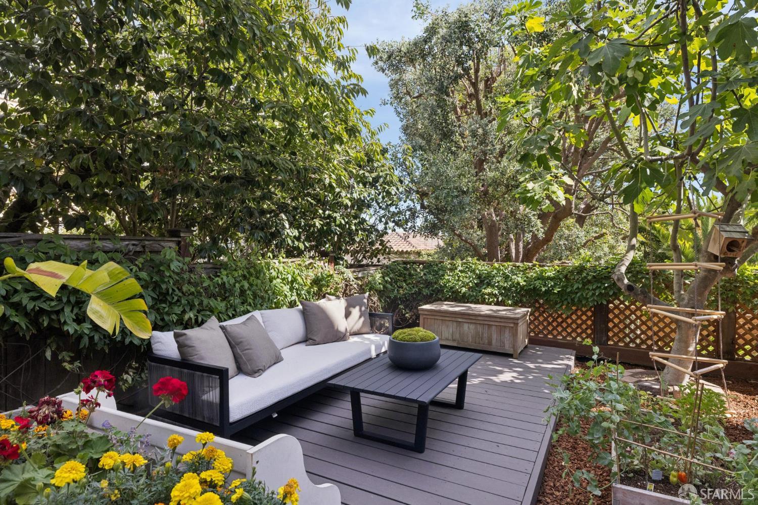 Garden deck with a gray sectional sofa, black coffee table, and colorful flower planters.