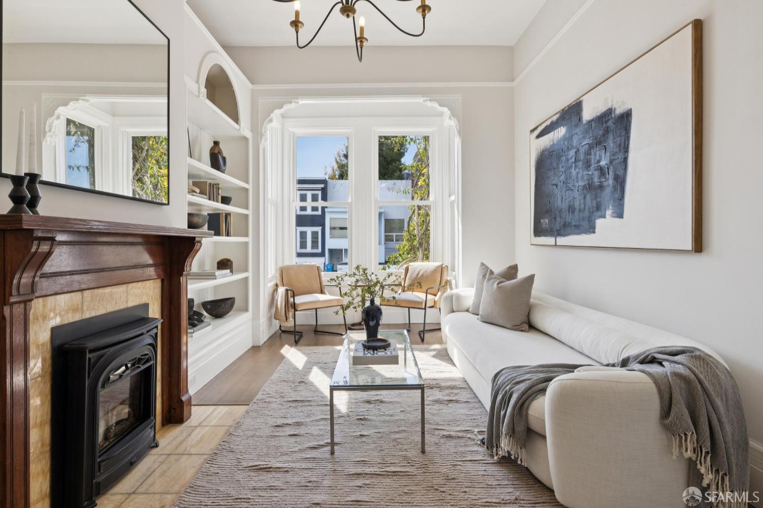 Staged living room with a white sofa, ornate fireplace, and tall bay windows.