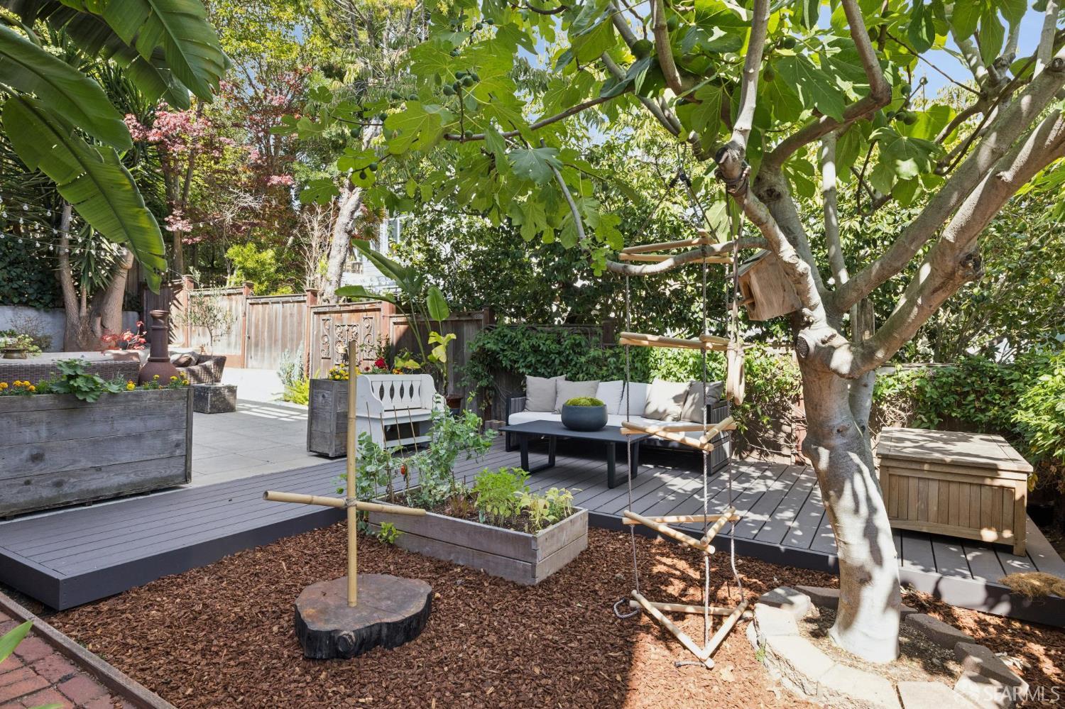 Landscaped backyard with a raised deck, outdoor lounge seating, and a swing beneath mature trees.