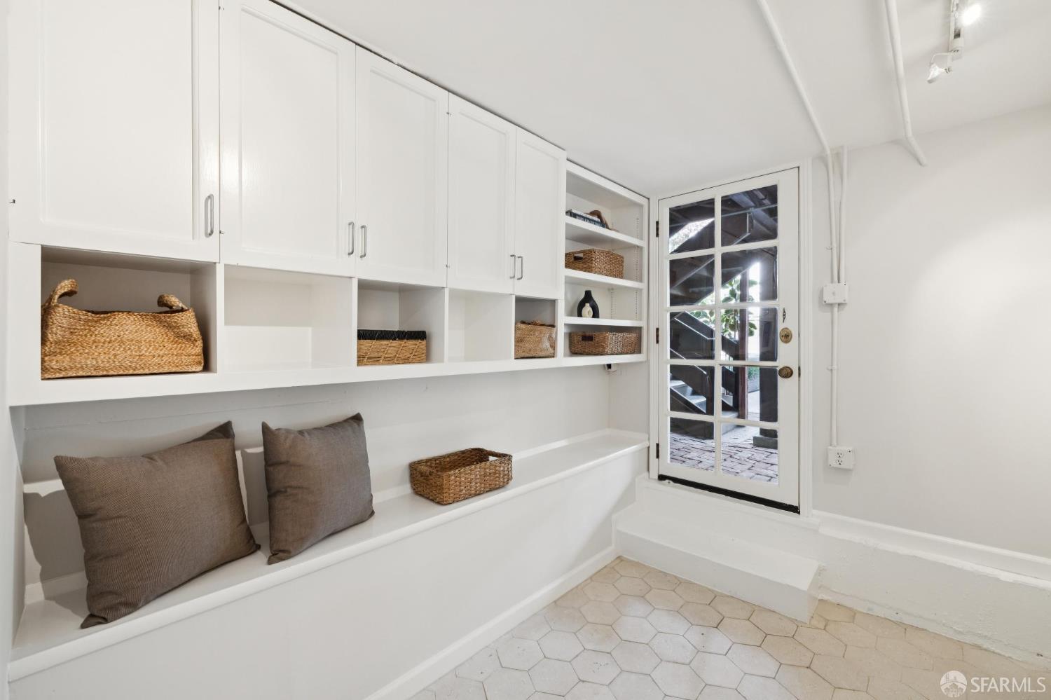 Mudroom with white built-in storage, a cushioned bench, hexagonal tile floor, and glass-paneled door.