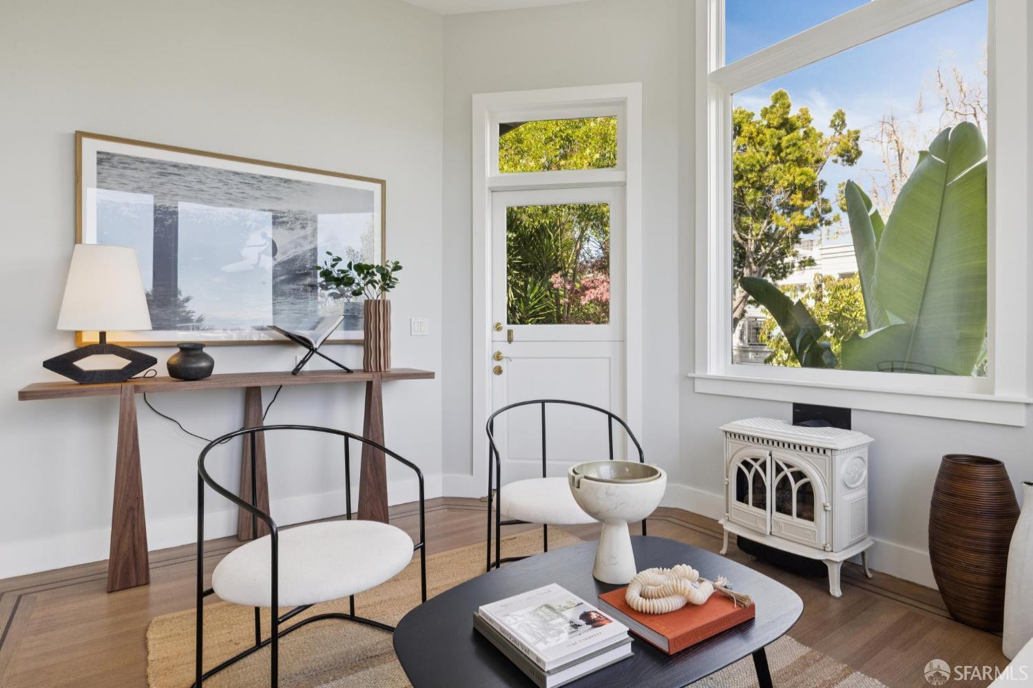 Staged living room with a large tree-framed window, hardwood floors, and a decorative white stove.