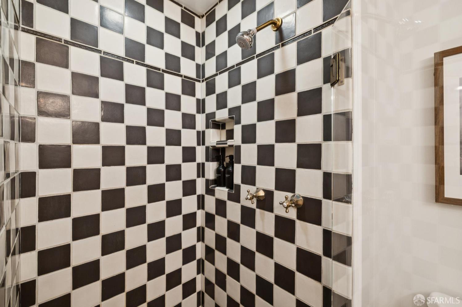 Tiled shower with black-and-white squares, brass fixtures, and a recessed niche.