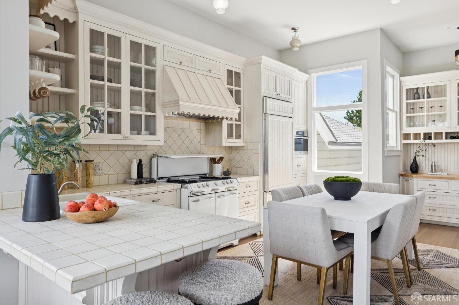 Bright kitchen and dining area with white cabinetry, tiled counters, and a table beside large windows.
