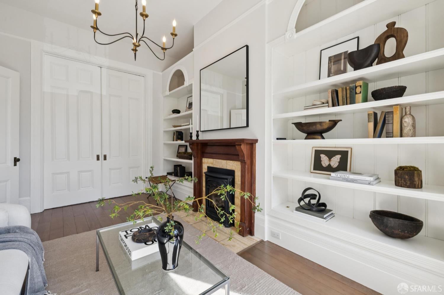 Living room with built-in white bookshelves, a wood fireplace mantel, and hardwood floors.