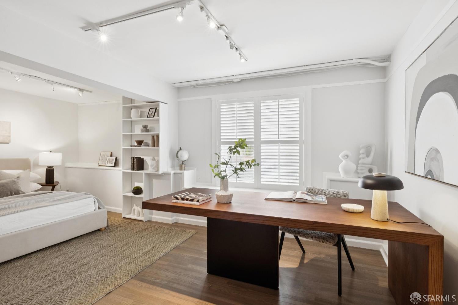 Staged bedroom and office with a large wood desk, built-in shelves, and shuttered windows.