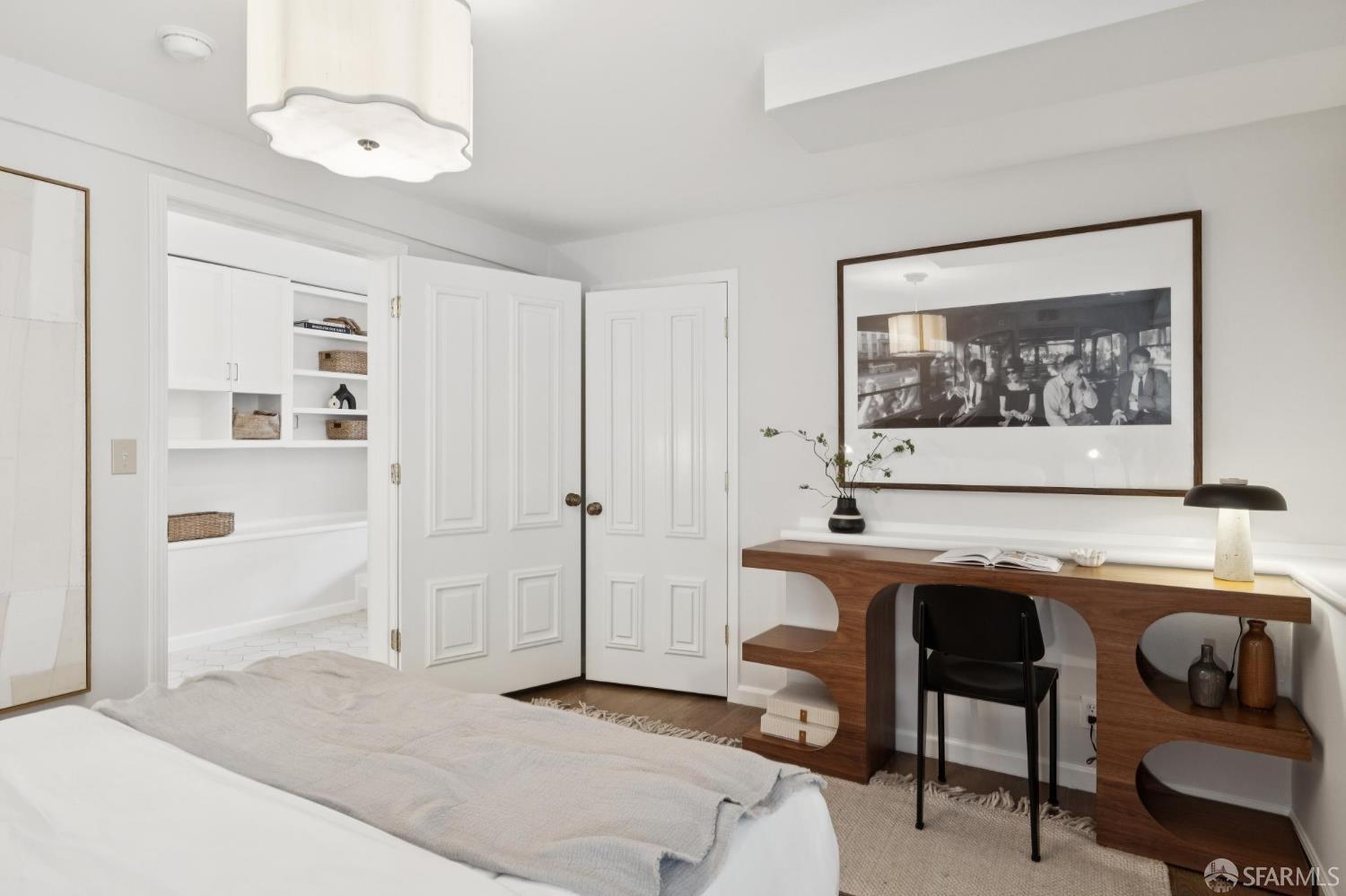 Bedroom with a sculptural walnut desk, black chair, and built-in closet with woven baskets.