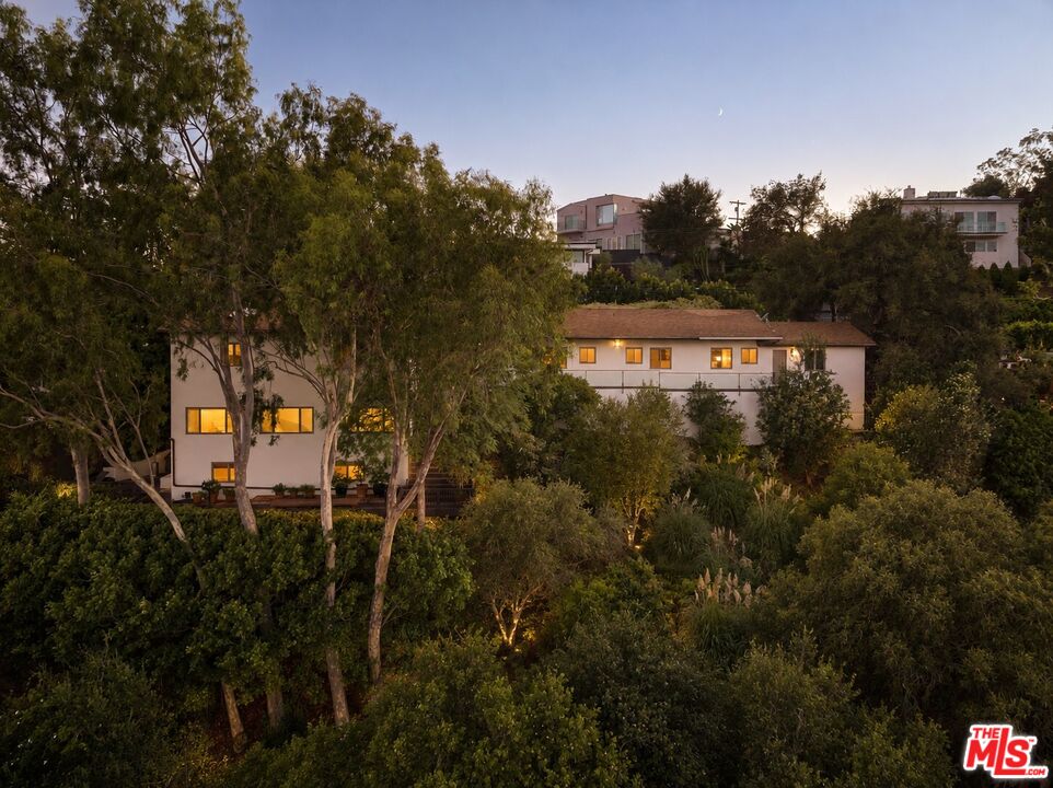 White multi-level home nestled among trees, its windows glowing at dusk.