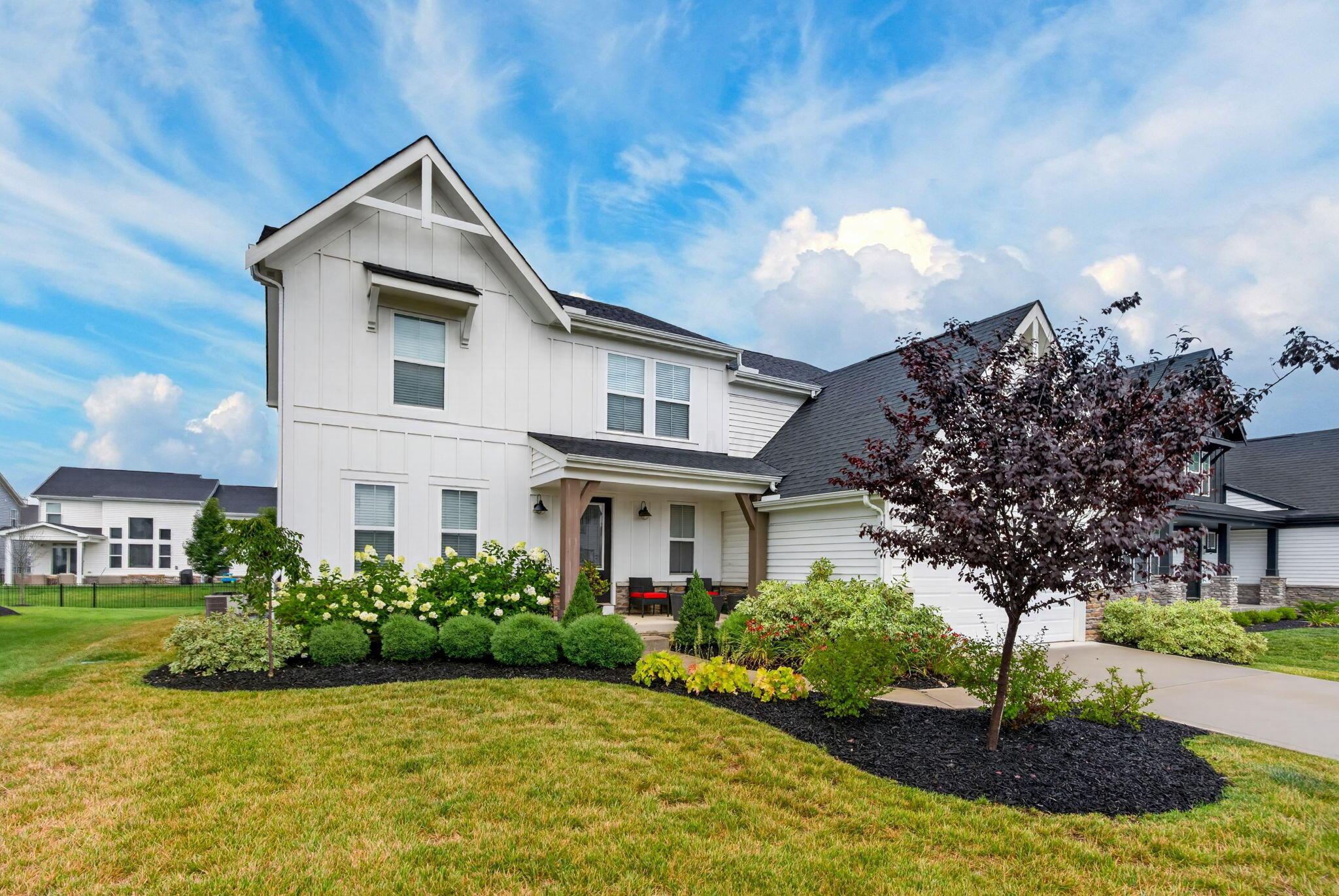 Two-story white house with a covered porch, attached garage, and landscaped front yard.