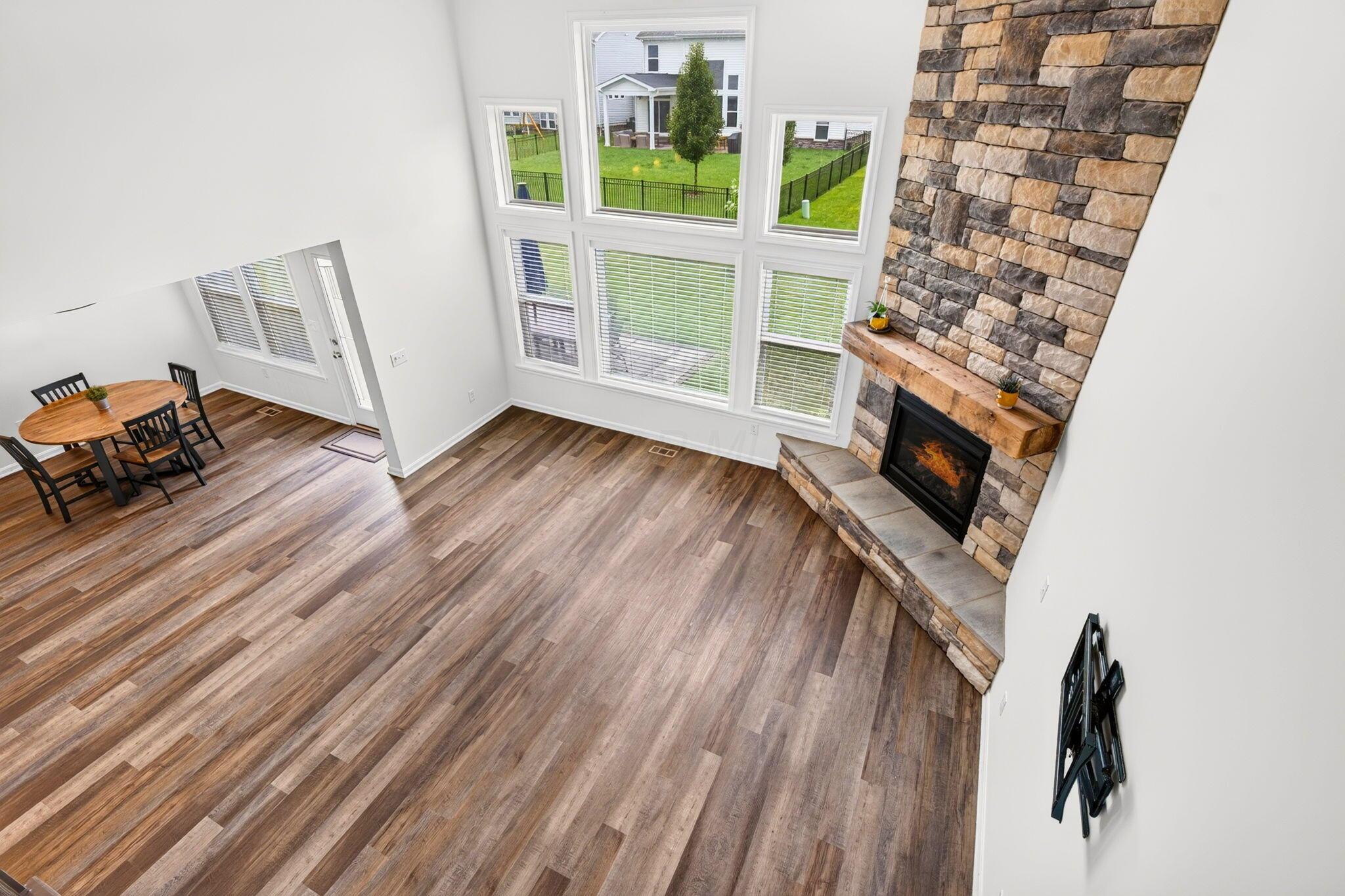 Living room with tall windows, a stone fireplace, and an adjoining dining area.