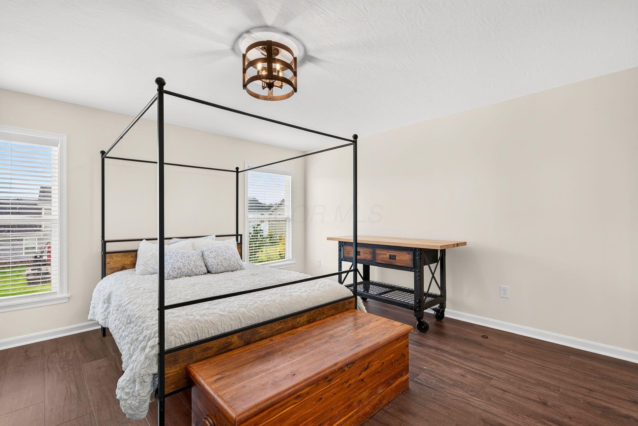 Bedroom with a black metal four-poster bed, white bedding, and warm wood furnishings.