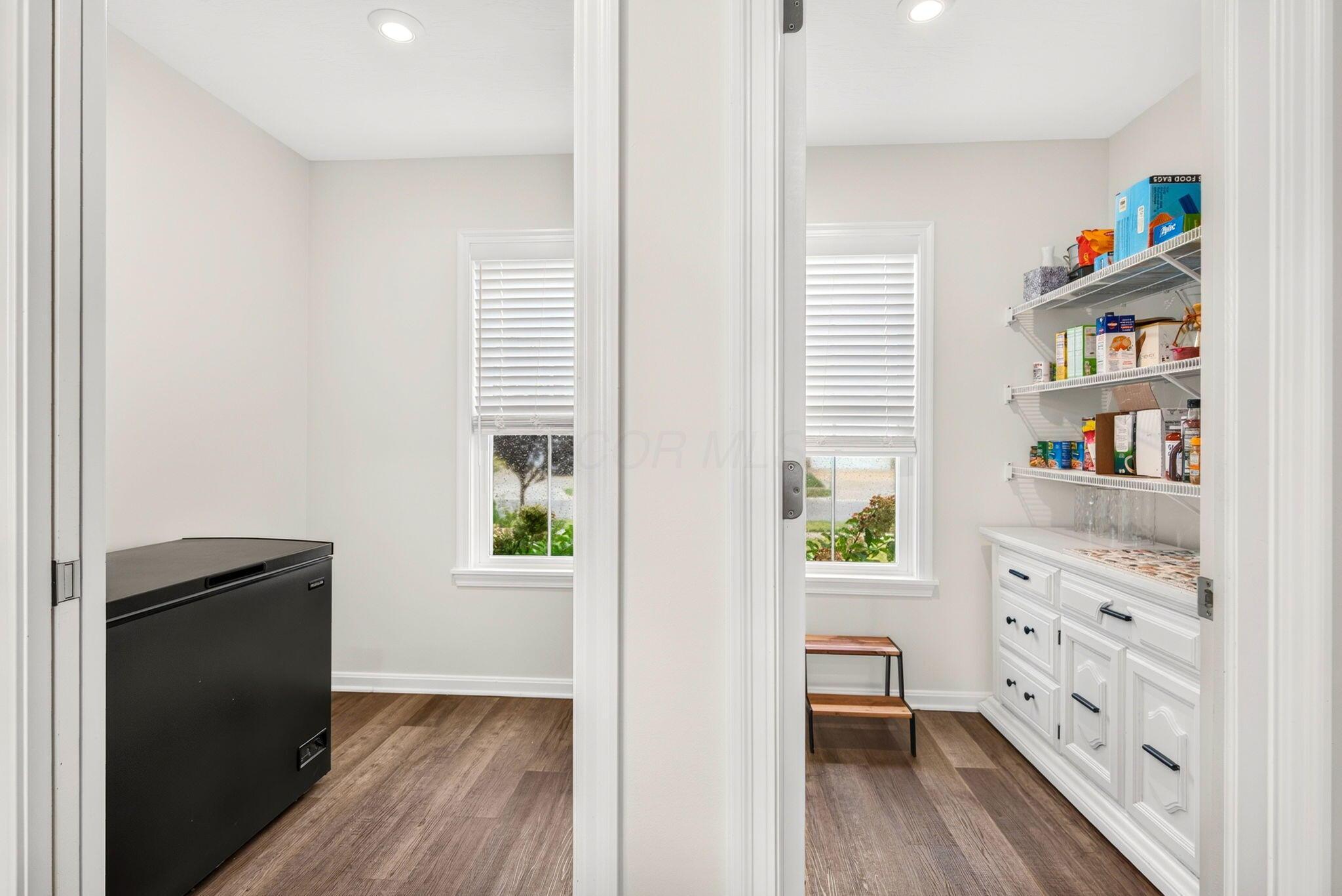 Pantry with white cabinets and stocked wire shelves, a black chest freezer, and two windows.
