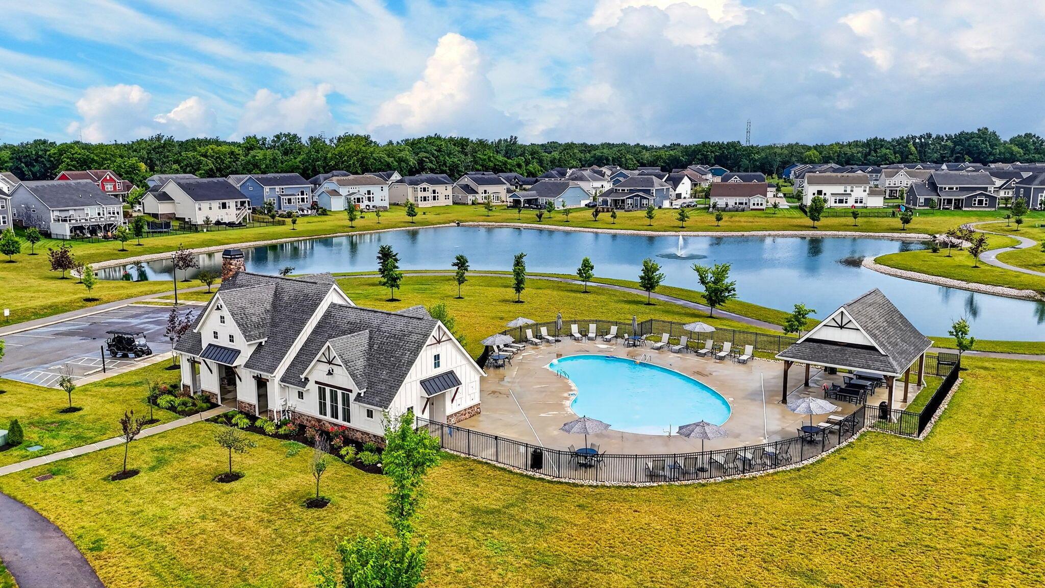 Aerial view of a community pond and pool, with a clubhouse, pavilion, and homes.