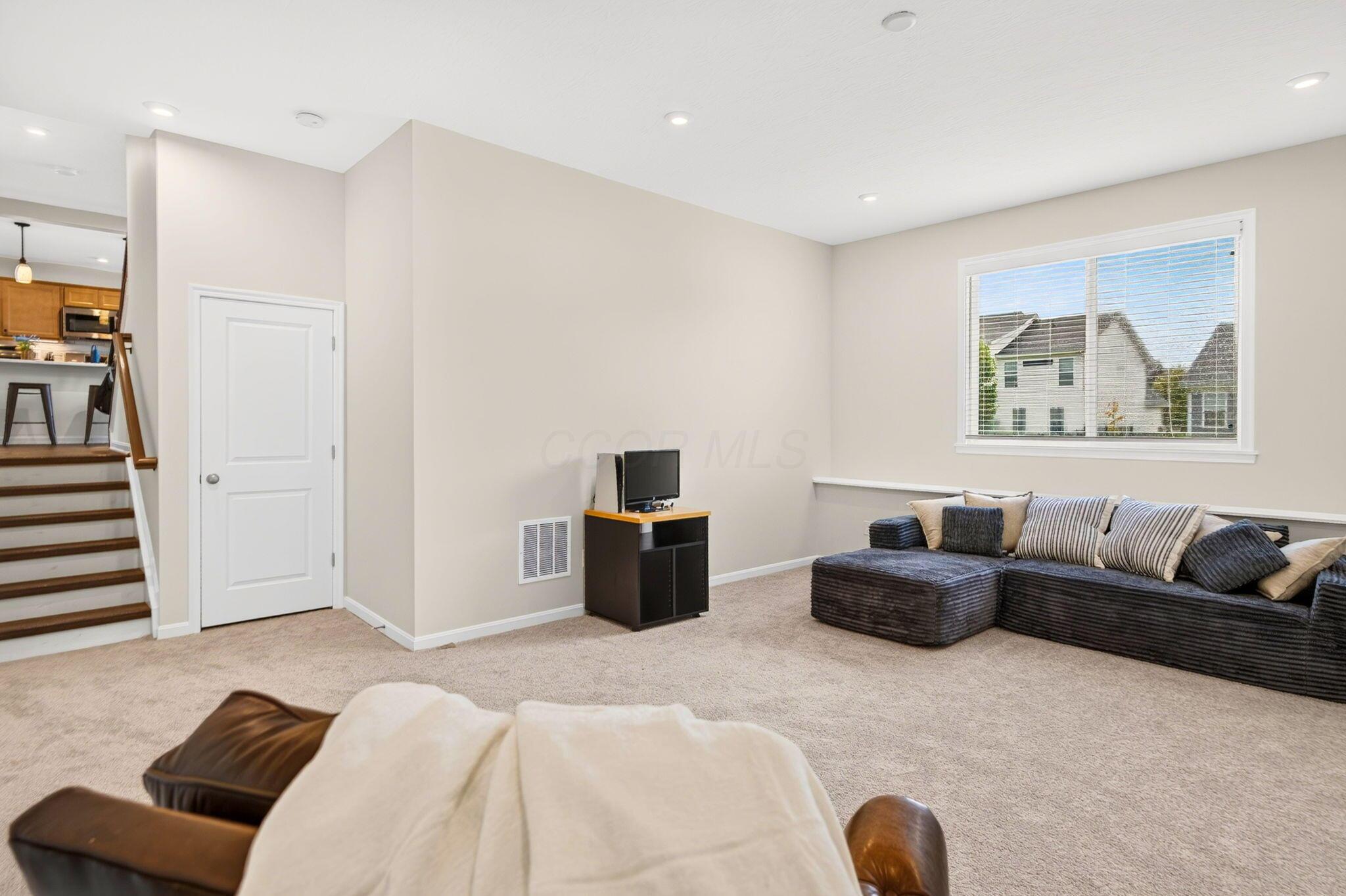 Living room with a dark sectional sofa, carpeted floor, and stairs beside the open kitchen.