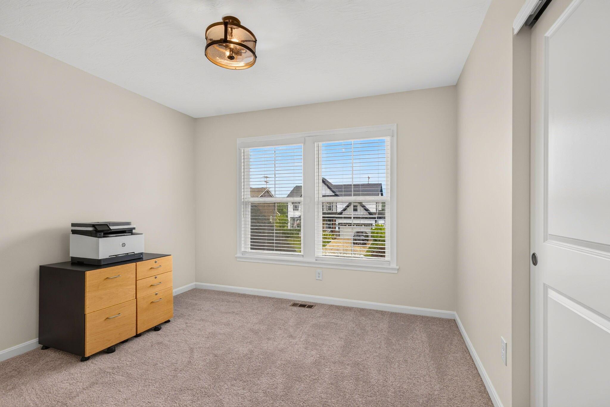Carpeted room with a printer on a cabinet beside a double window with blinds.