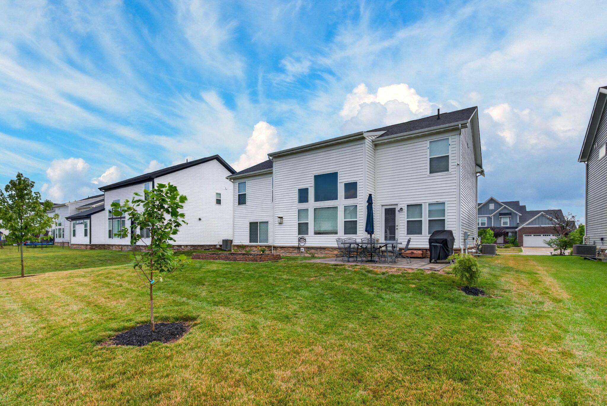 Rear of a two-story white house with a patio, lawn, and young trees.