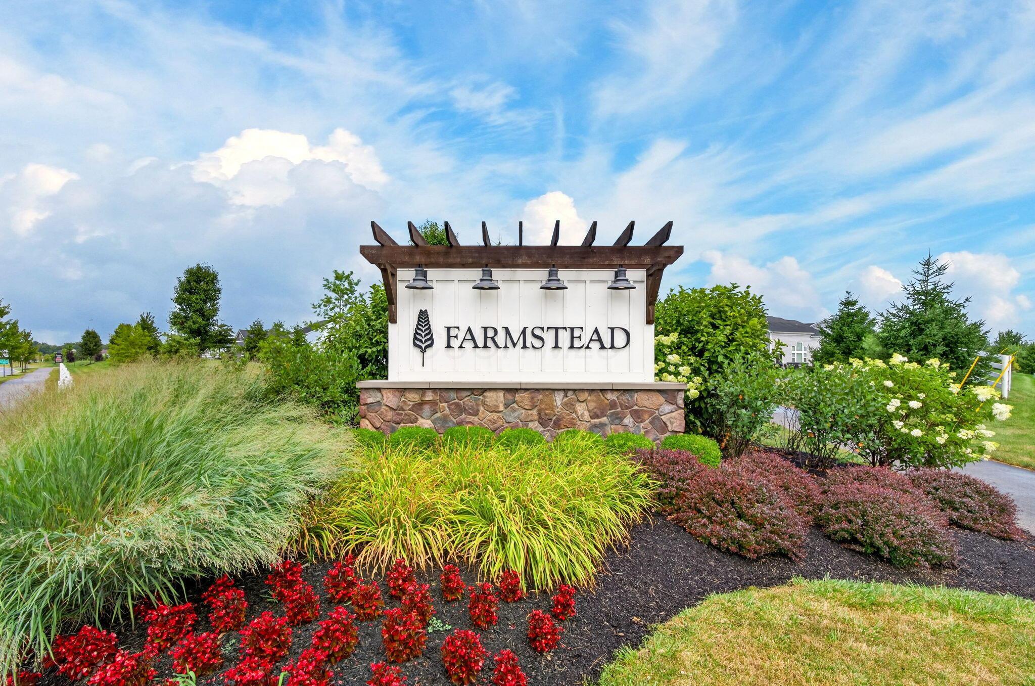 Farmstead community entrance sign amid colorful flower beds and ornamental grasses.