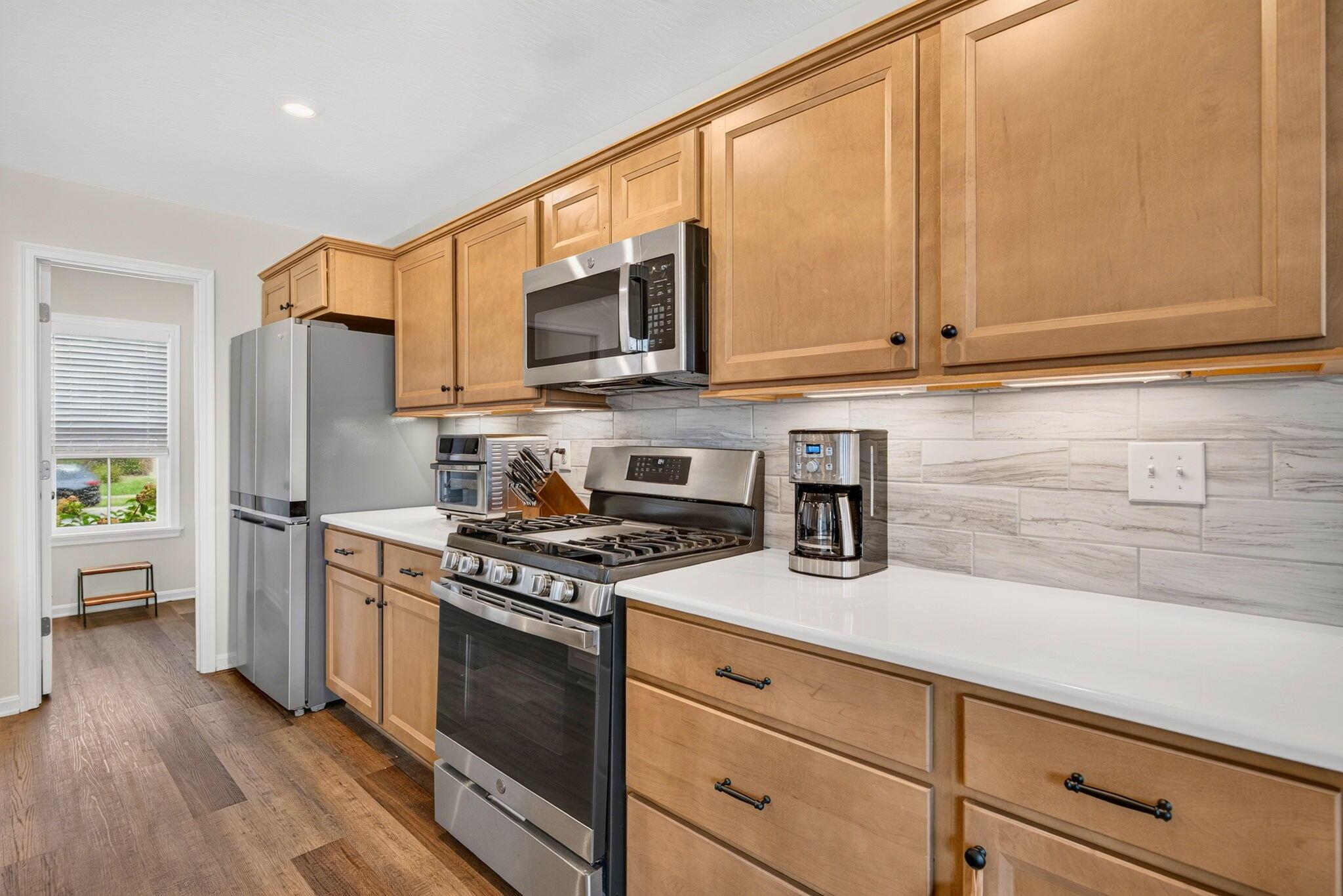 Kitchen with wood cabinets, stainless steel appliances, white counters, and a light tile backsplash.