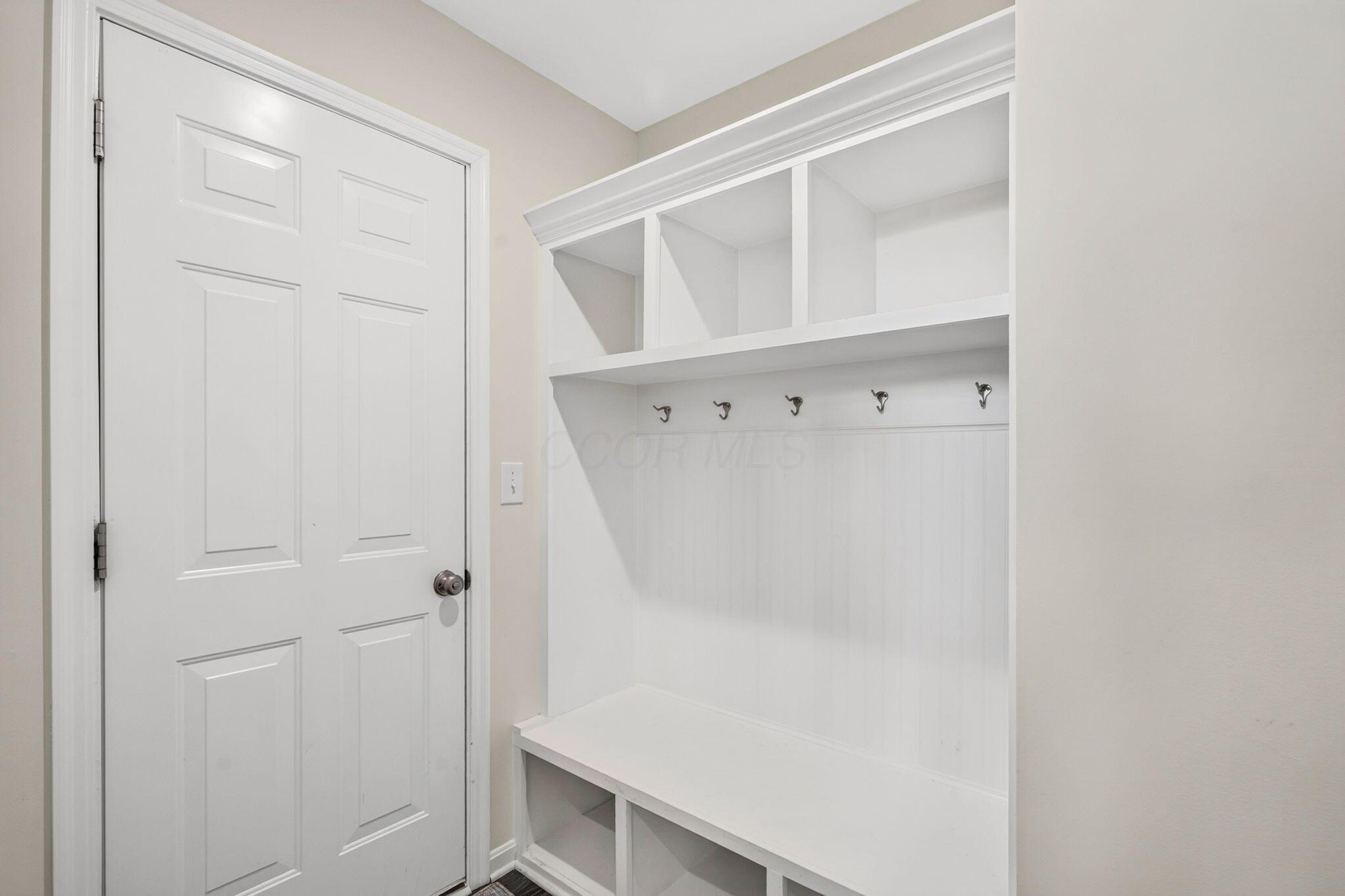 Mudroom with a white built-in bench, storage cubbies, and coat hooks beside the entry door.