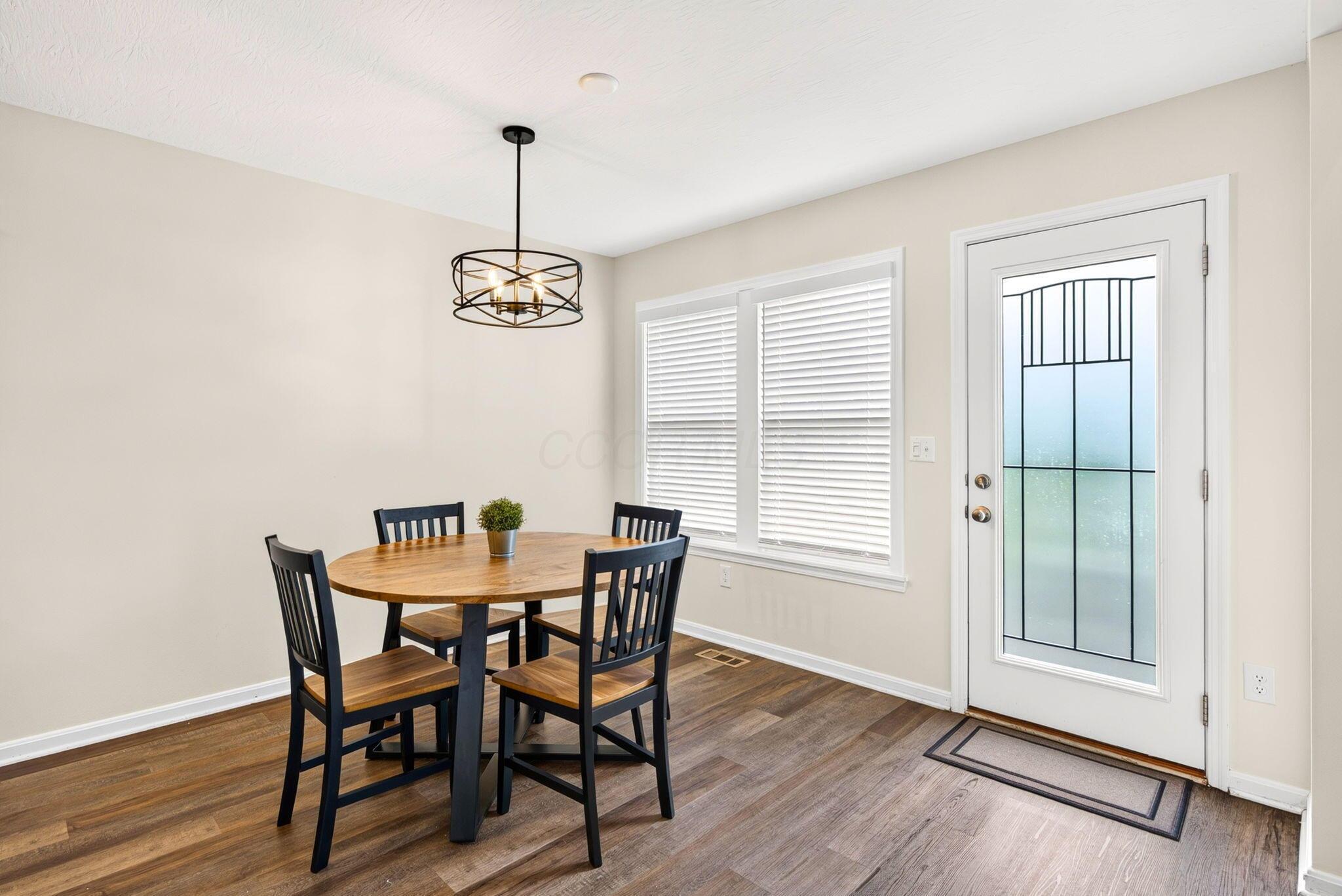 Dining area with a round wooden table, four dark chairs, and a glass-paneled exterior door.