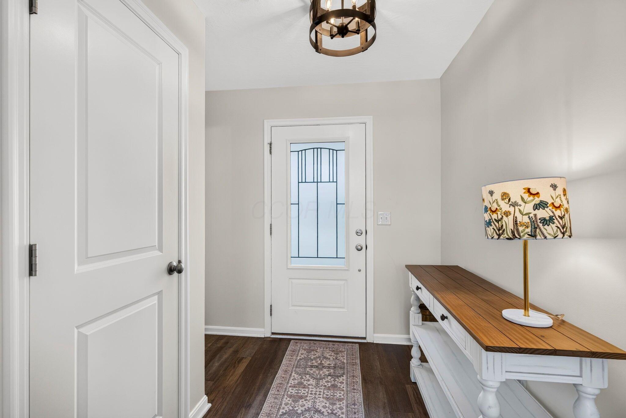 Entryway with a decorative glass front door, patterned runner, and white console table with a floral lamp.