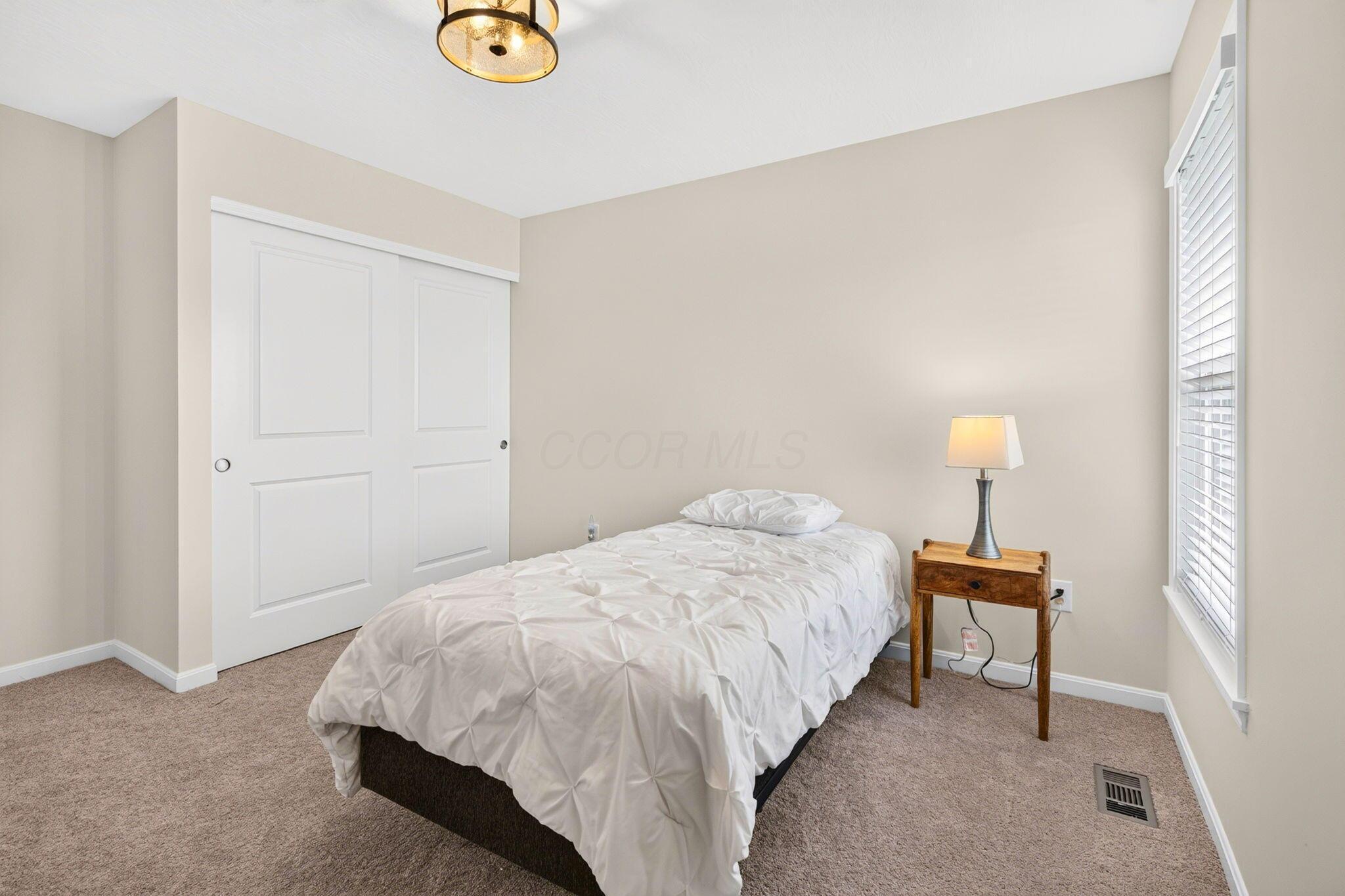 Furnished bedroom with a white bed, sliding closet doors, and a window with blinds.