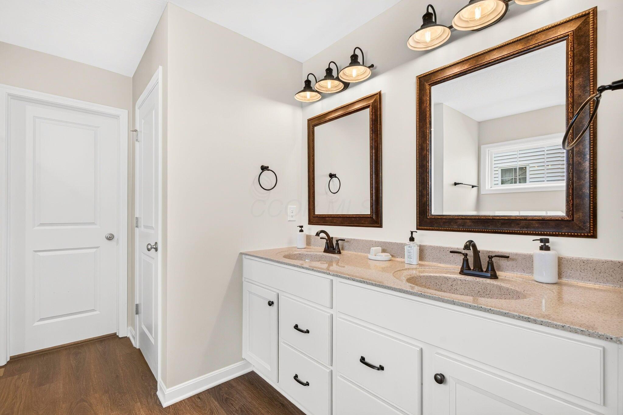 Bathroom with a double-sink vanity, speckled countertop, dark faucets, and two framed mirrors.